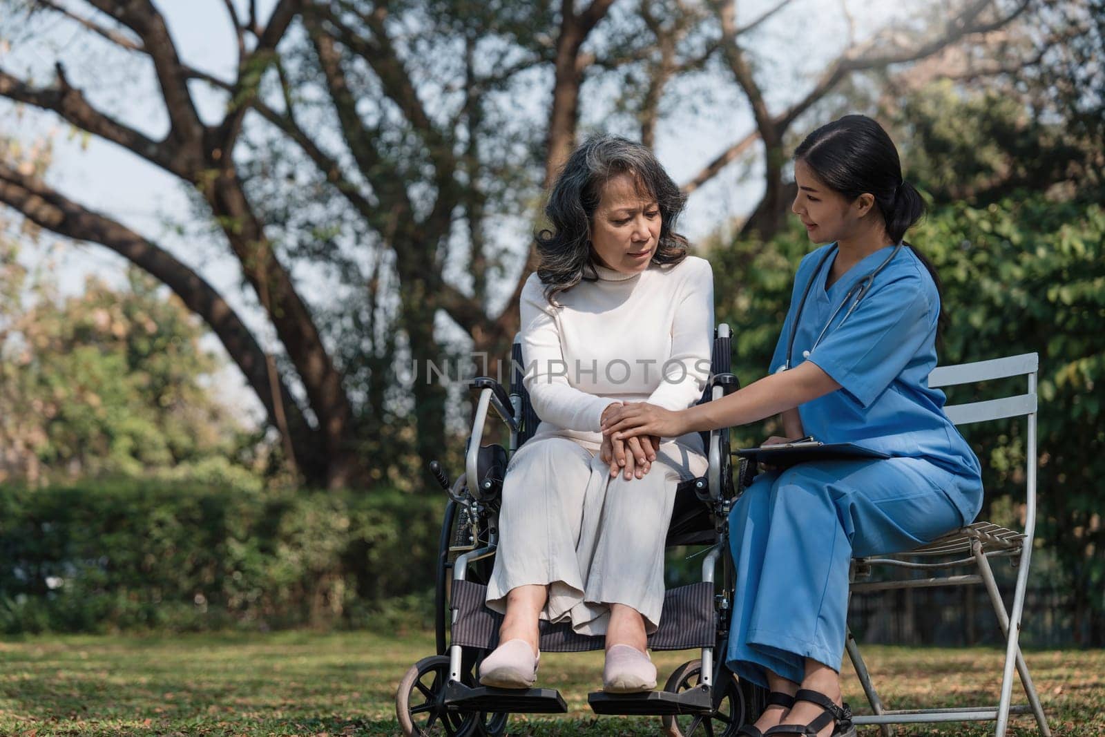 Female nurse doing blood pressure measurement of a senior woman patient. Doctor checking blood pressure of an elderly woman at garden home. Female caregiver and senior woman together