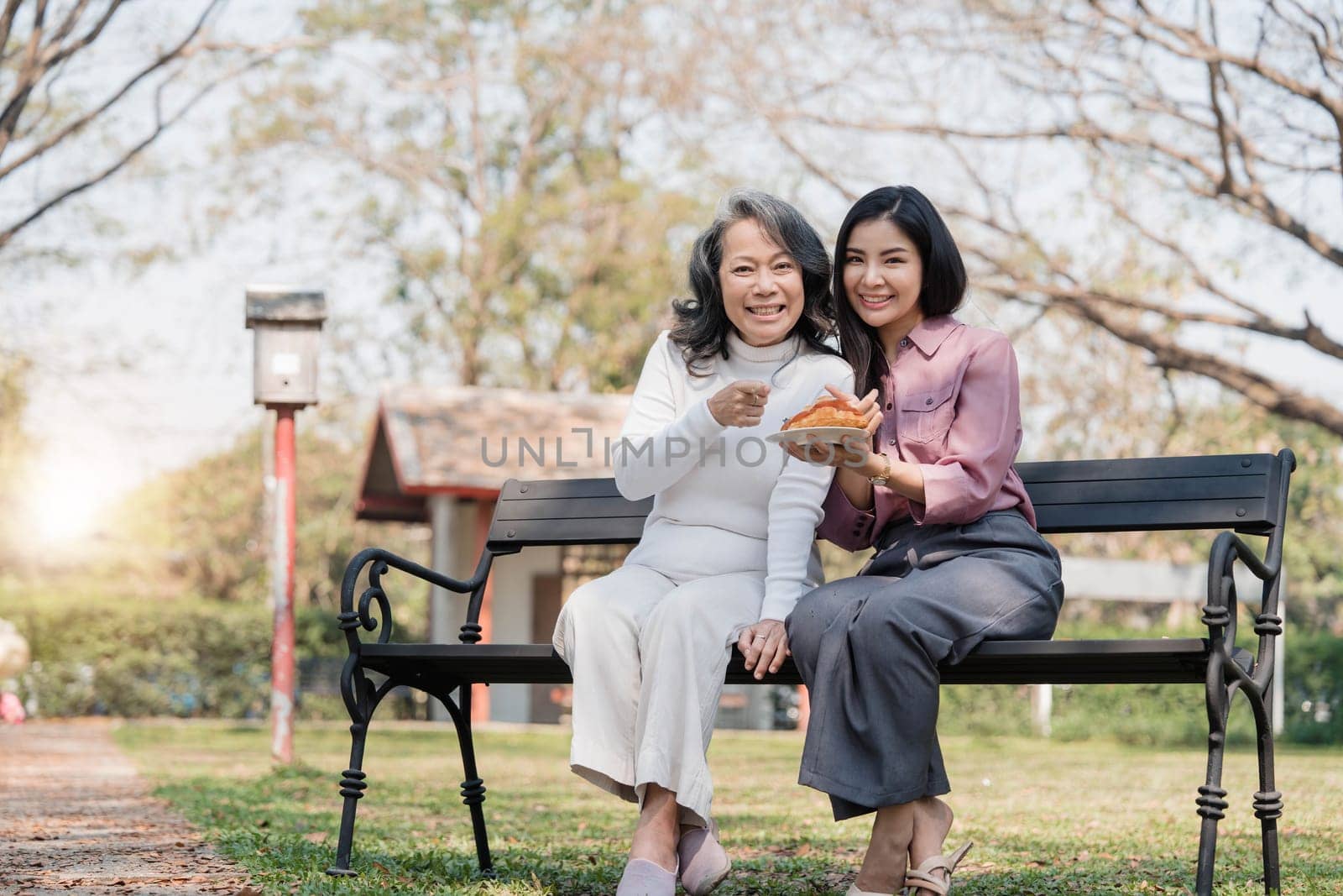 Happy adult granddaughter and senior grandmother having fun enjoying talk sit with green nature. in park..