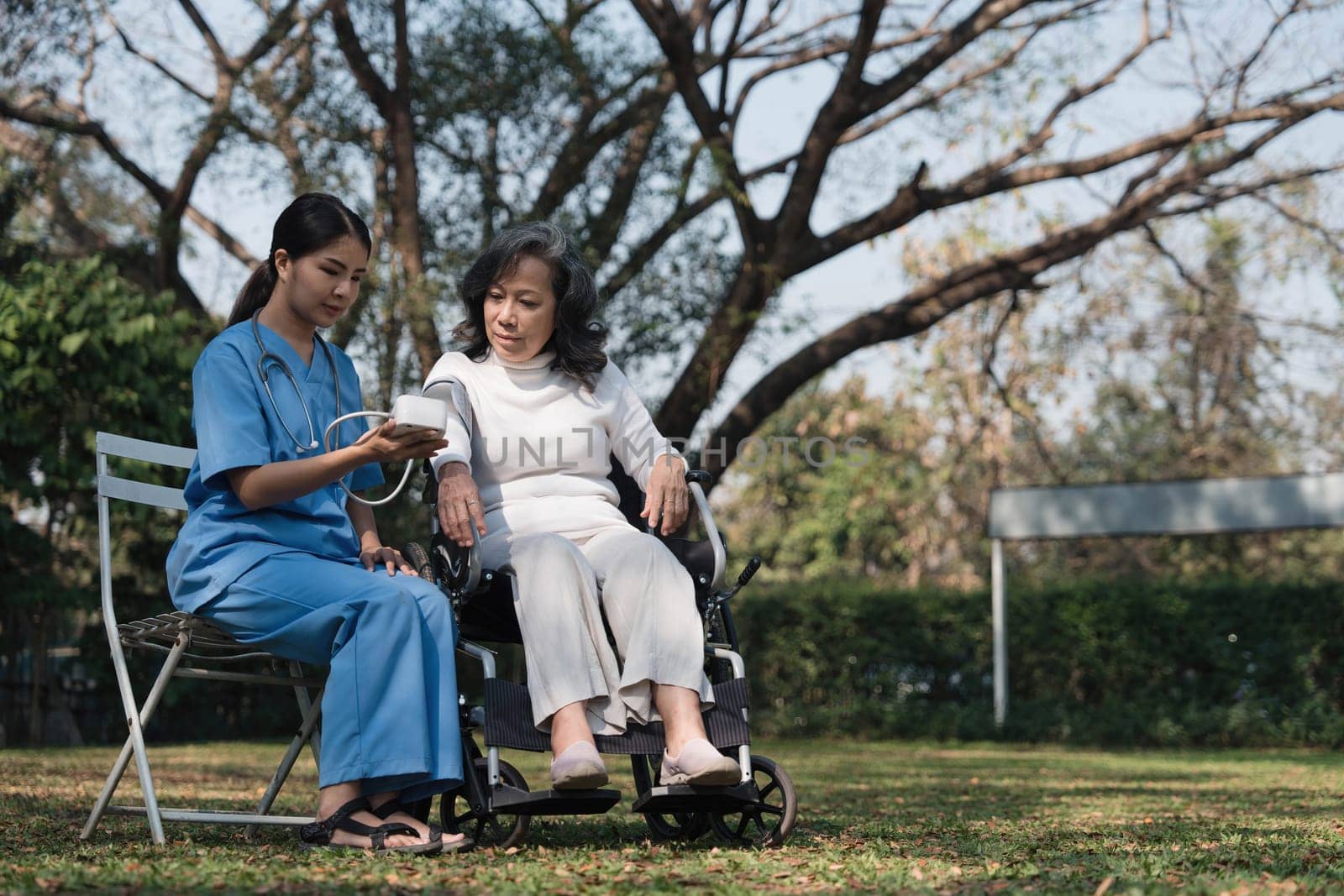 Female nurse doing blood pressure measurement of a senior woman patient. Doctor checking blood pressure of an elderly woman at garden home. Female caregiver and senior woman together