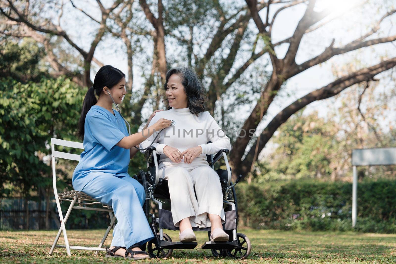 Female nurse doing blood pressure measurement of a senior woman patient. Doctor checking blood pressure of an elderly woman at garden home. Female caregiver and senior woman together