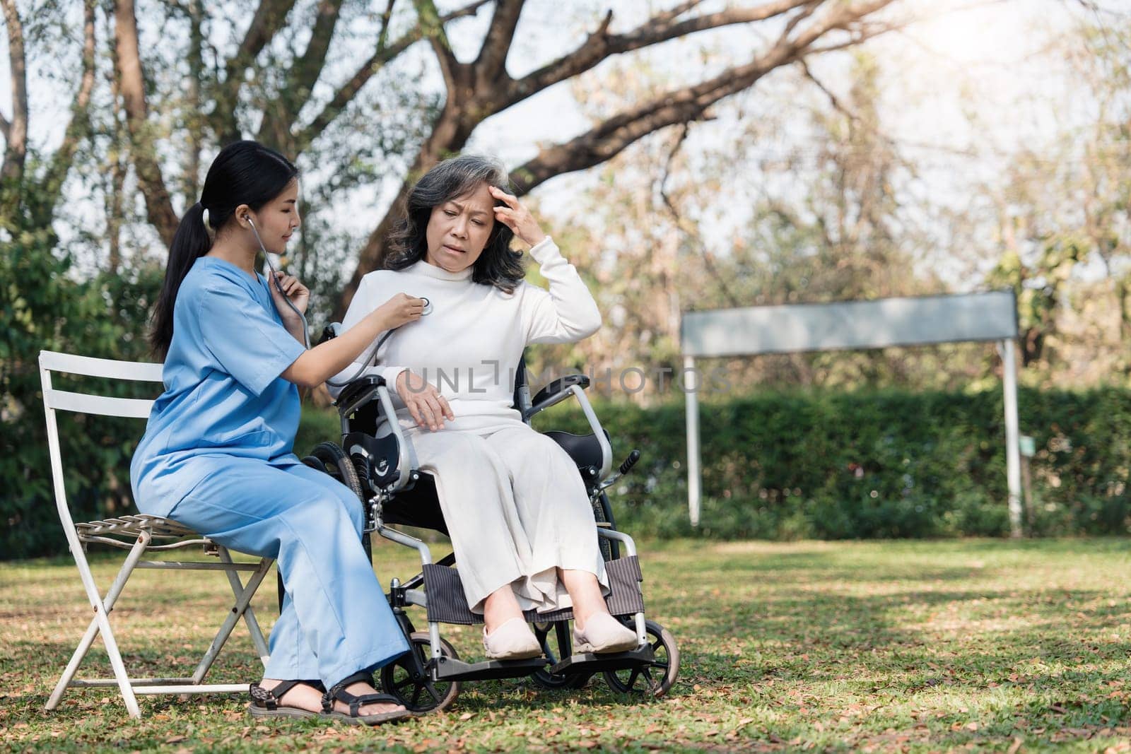 Female nurse doing blood pressure measurement of a senior woman patient. Doctor checking blood pressure of an elderly woman at garden home. Female caregiver and senior woman together