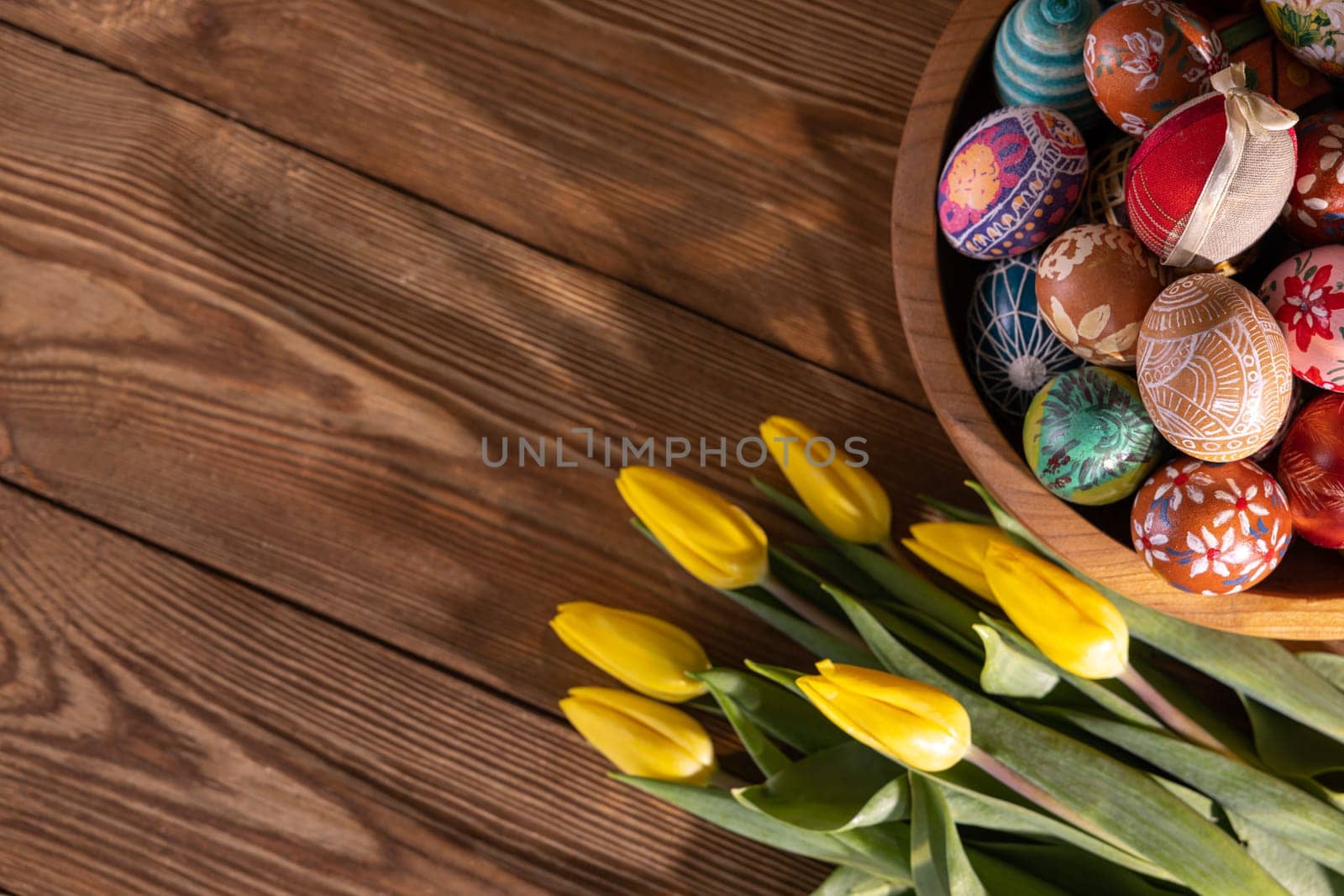 Hand-painted Easter eggs stacked on top of each other in a wooden bowl. Easter decoration as a base for your own composition or graphic inscriptions.