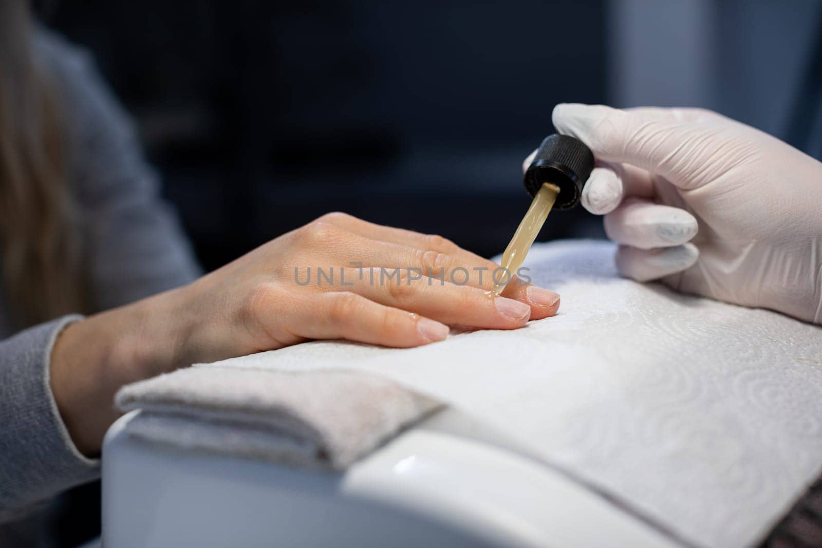 The professional nourishes the client's nails with cosmetic oil. The beautician wears disposable nitrile gloves. Maintaining the rules of hygiene in the beauty salon.