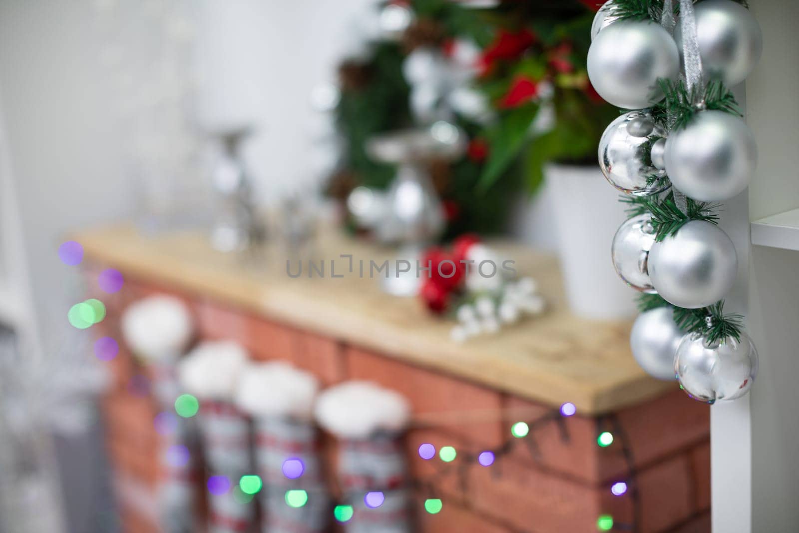 Silver baubles on spruce twigs and decorated fireplace in background.