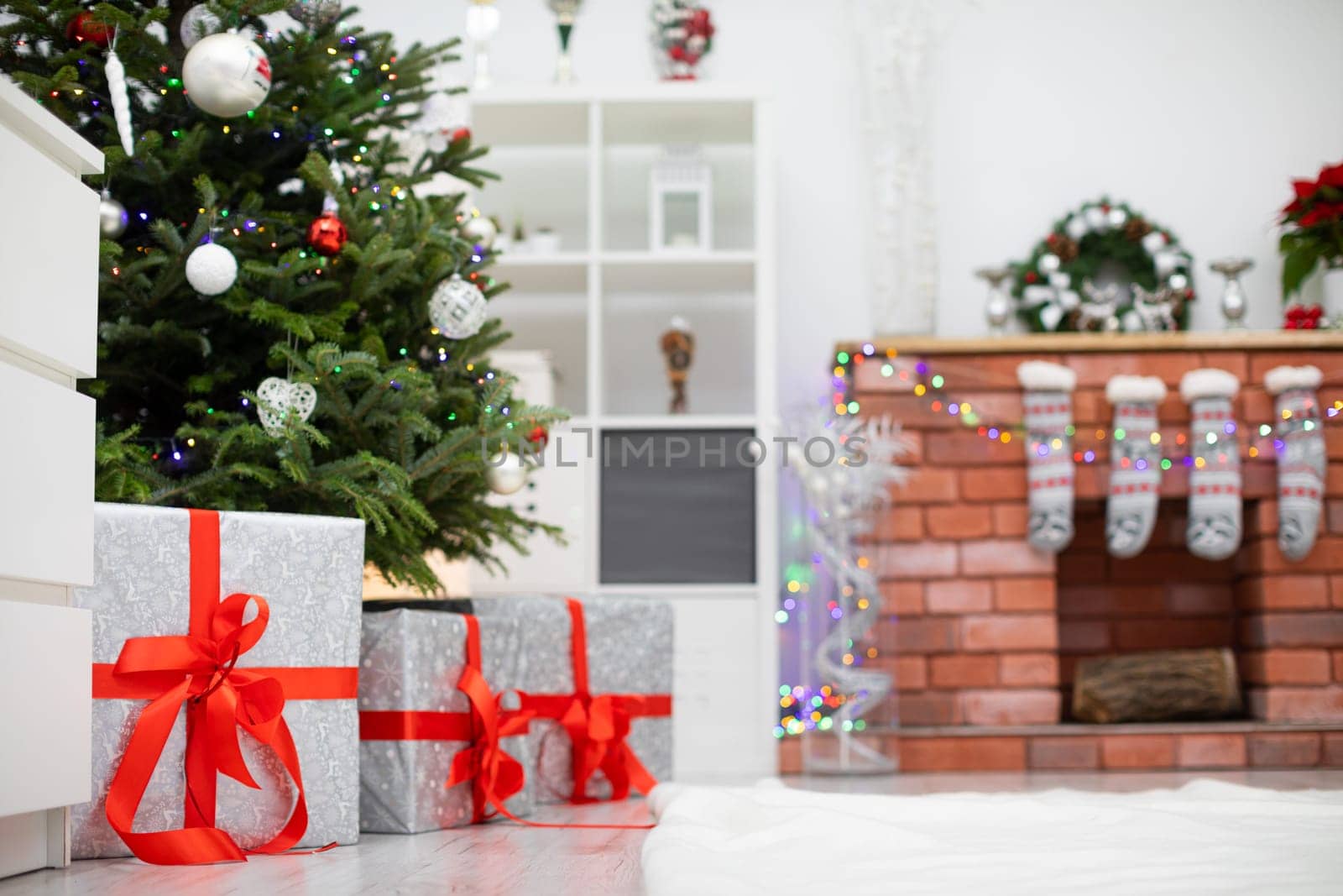 Decorated room with gifts under the Christmas tree. Fireplace with decorations in background.
