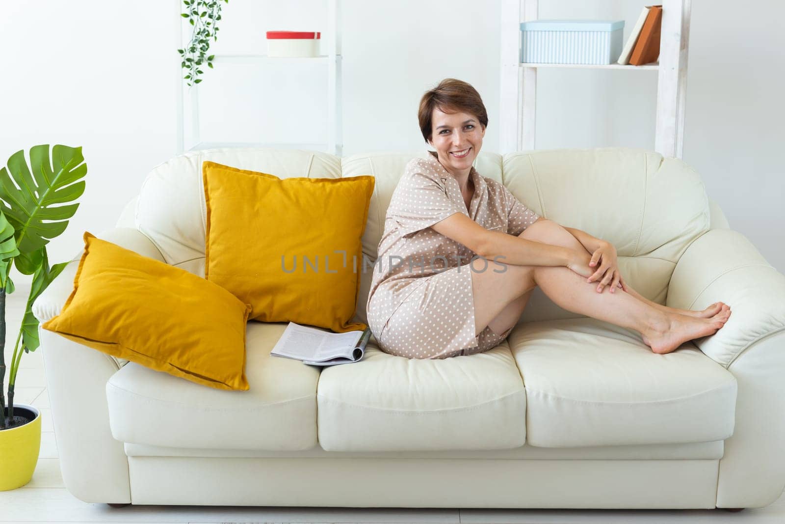 Woman wears pajama sitting on sofa in living room. Homewear, sleepwear, shopping and sale by Satura86