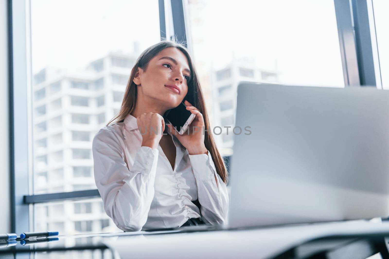 Young woman in white formal clothes is indoors in the modern office.