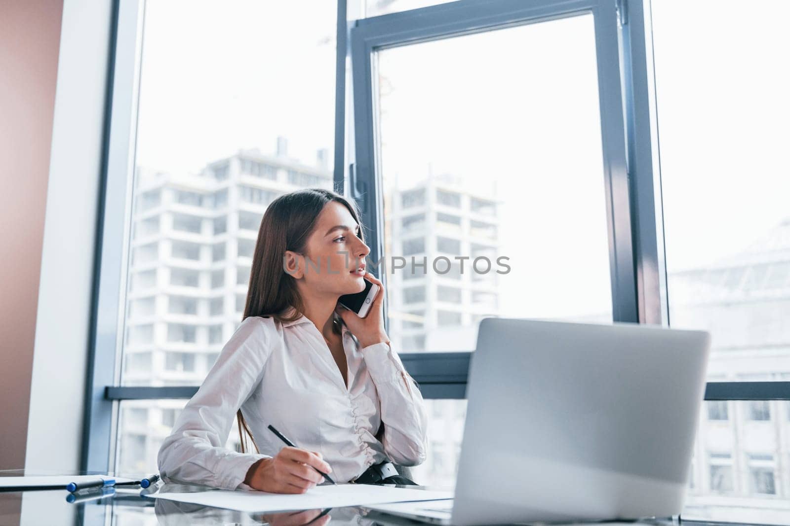 Young woman in white formal clothes is indoors in the modern office.