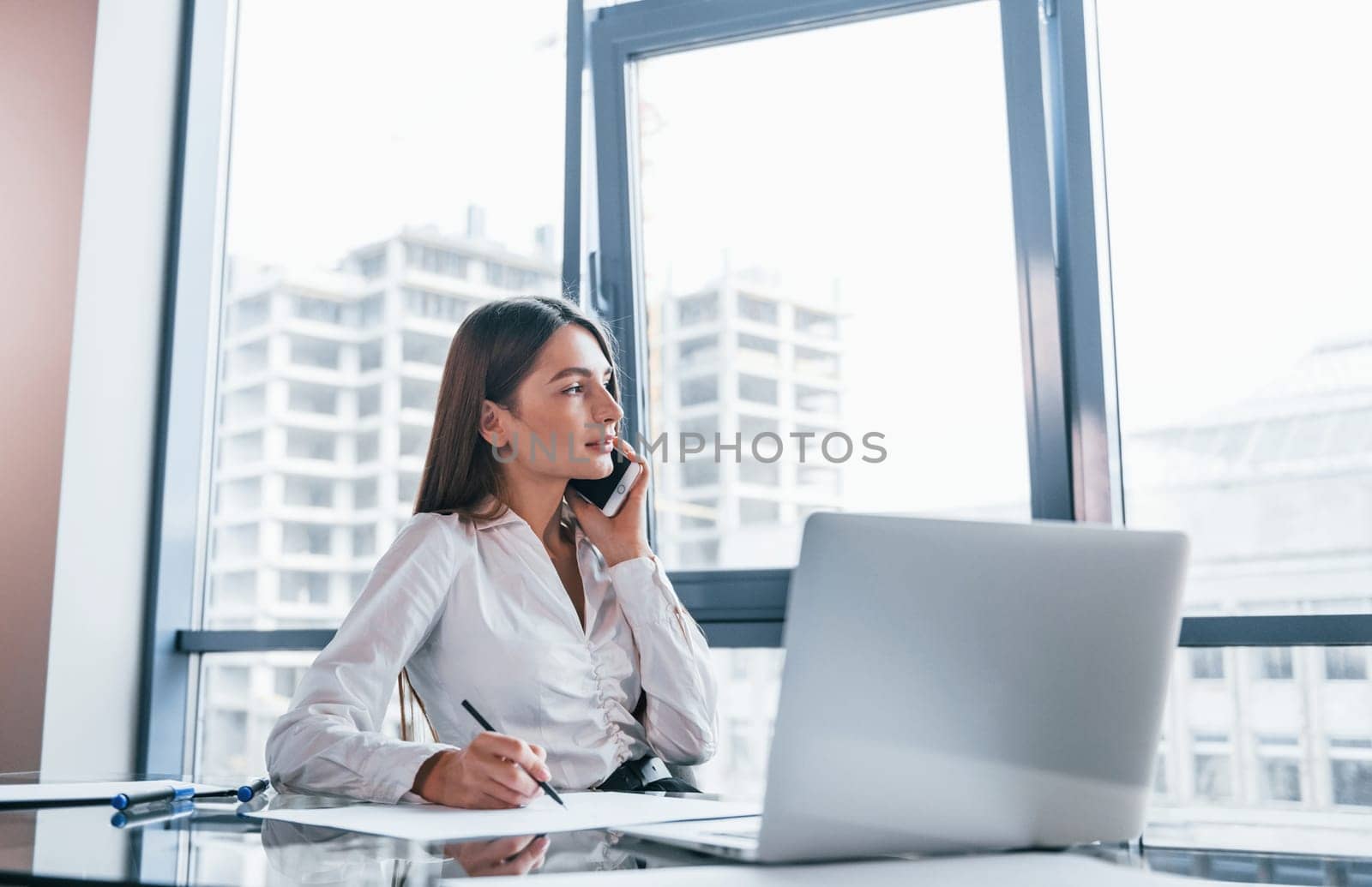 Young woman in white formal clothes is indoors in the modern office.
