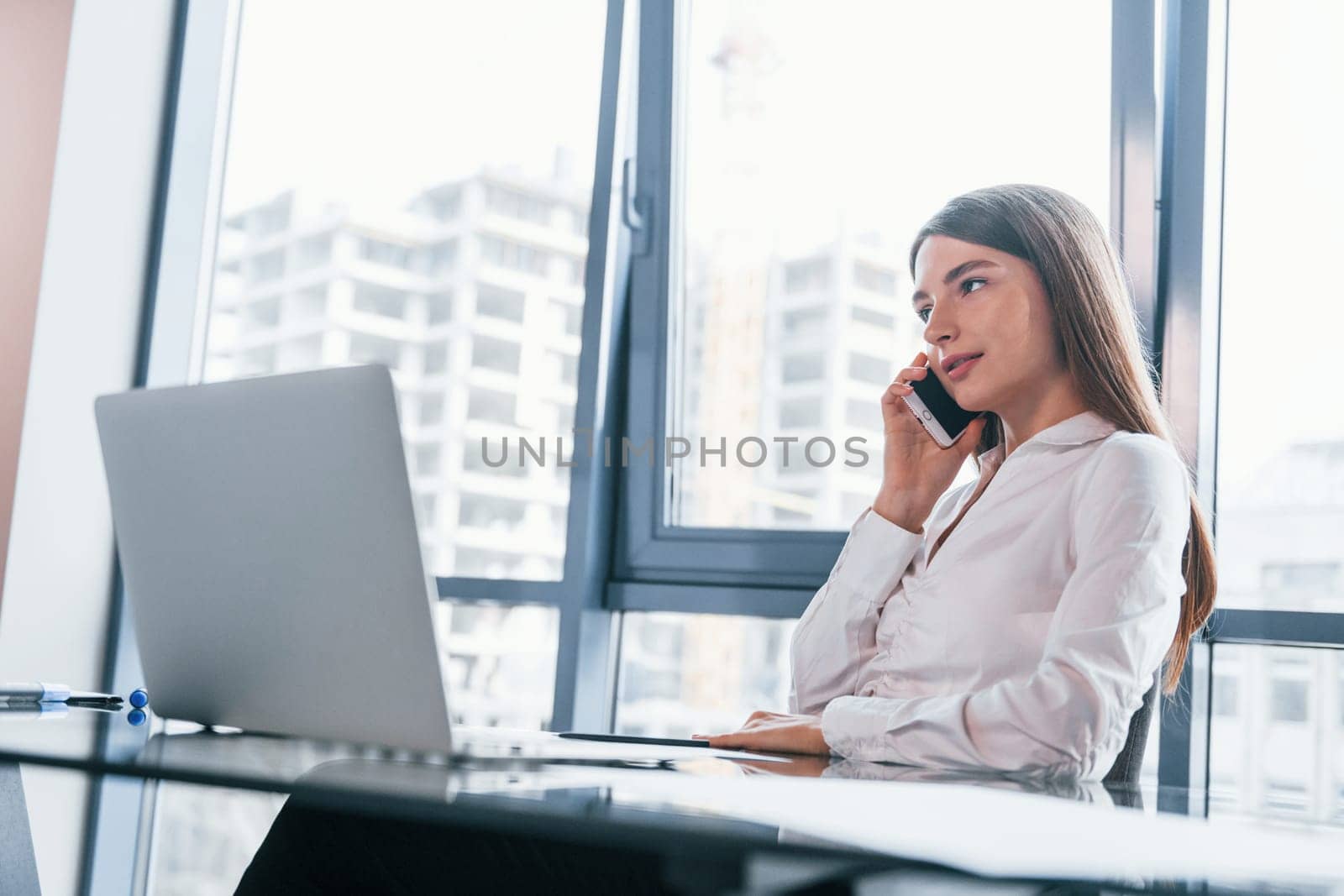 Busy day. Young woman in white formal clothes is indoors in the modern office.