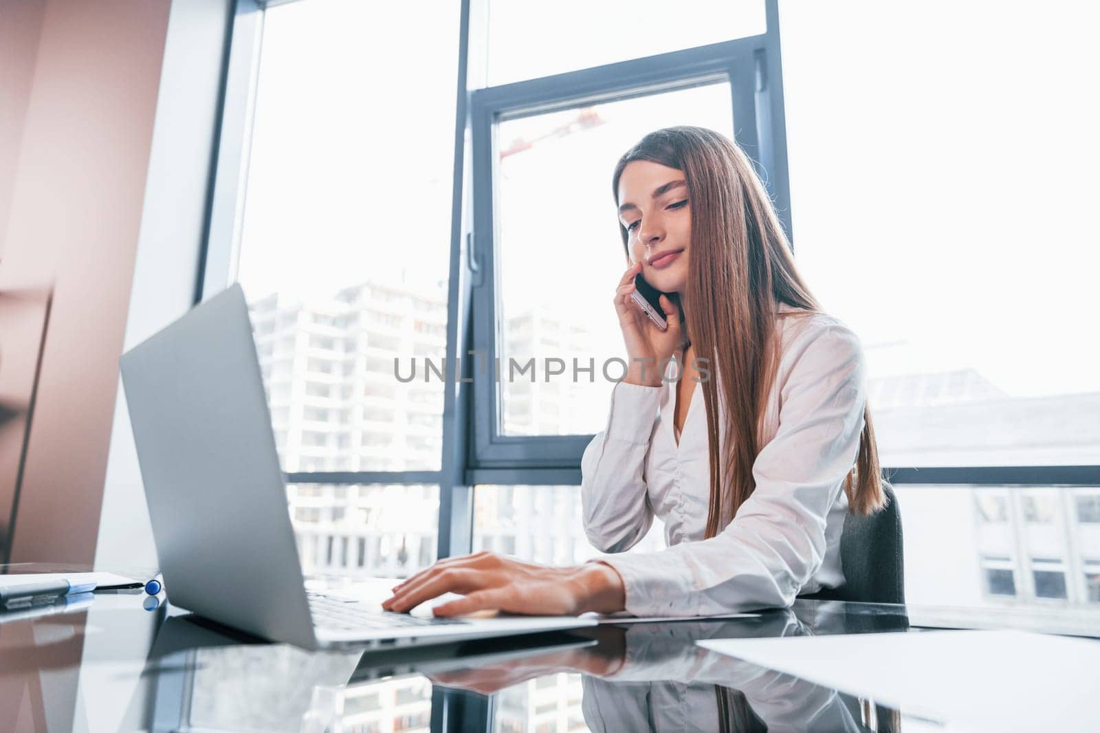 Busy day. Young woman in white formal clothes is indoors in the modern office.