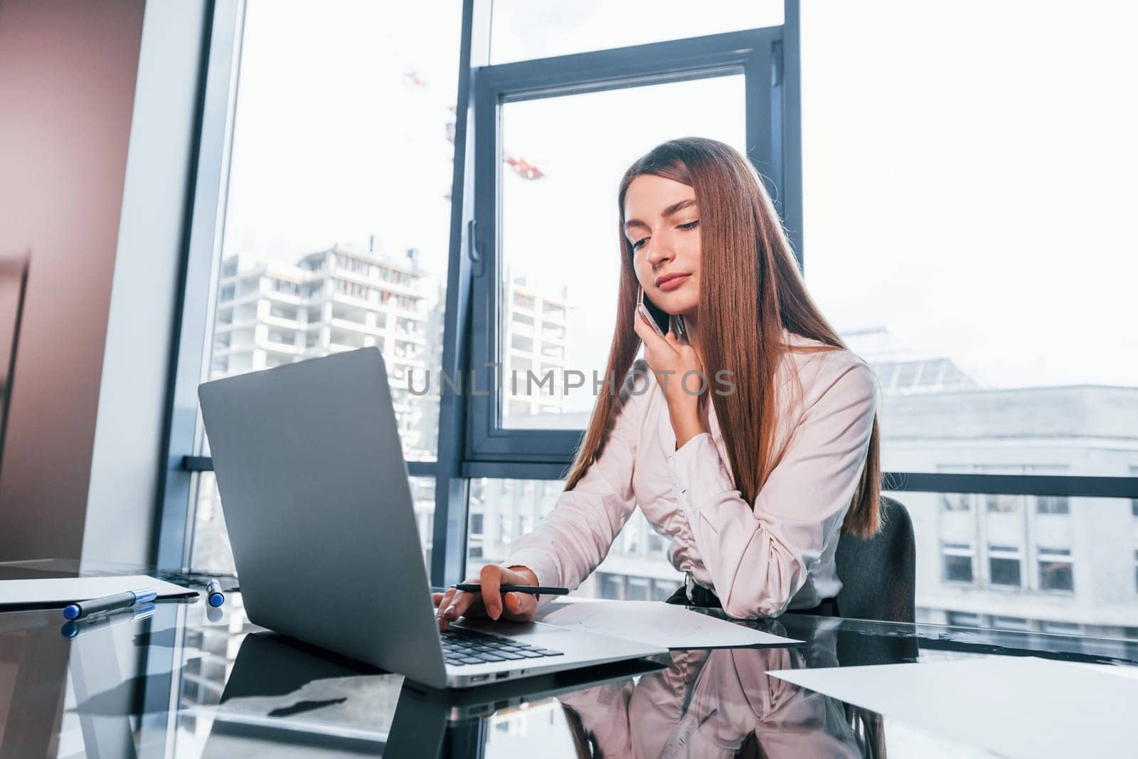 Busy day. Young woman in white formal clothes is indoors in the modern office.