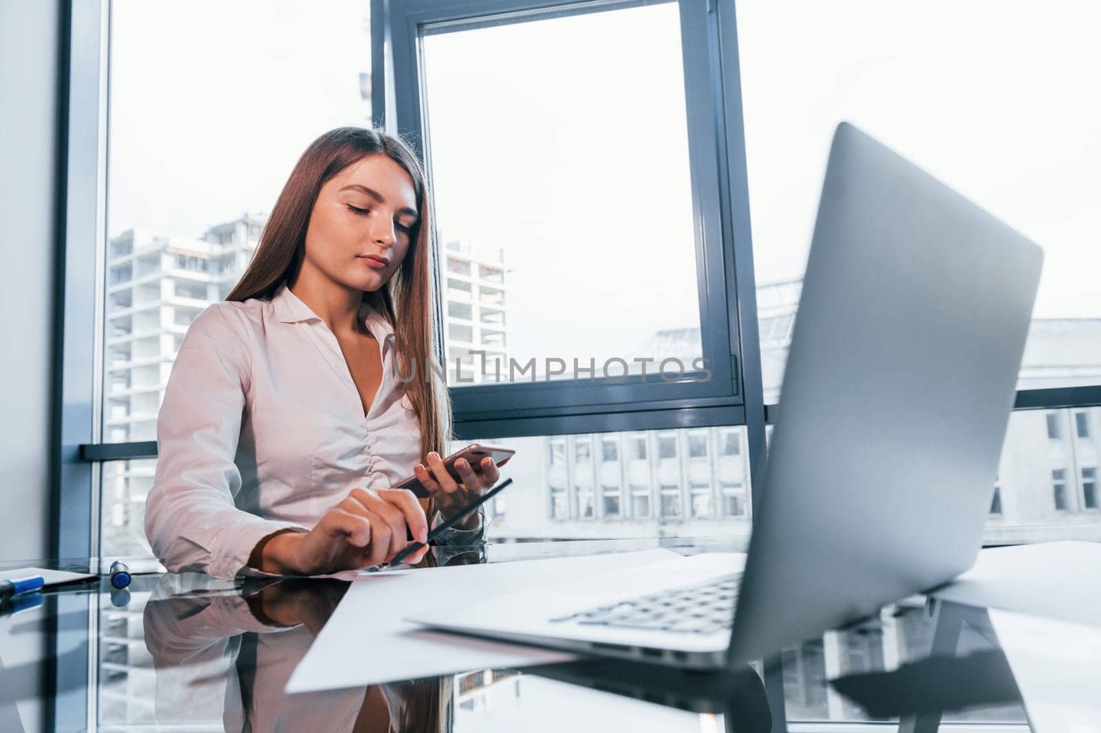 Busy day. Young woman in white formal clothes is indoors in the modern office.
