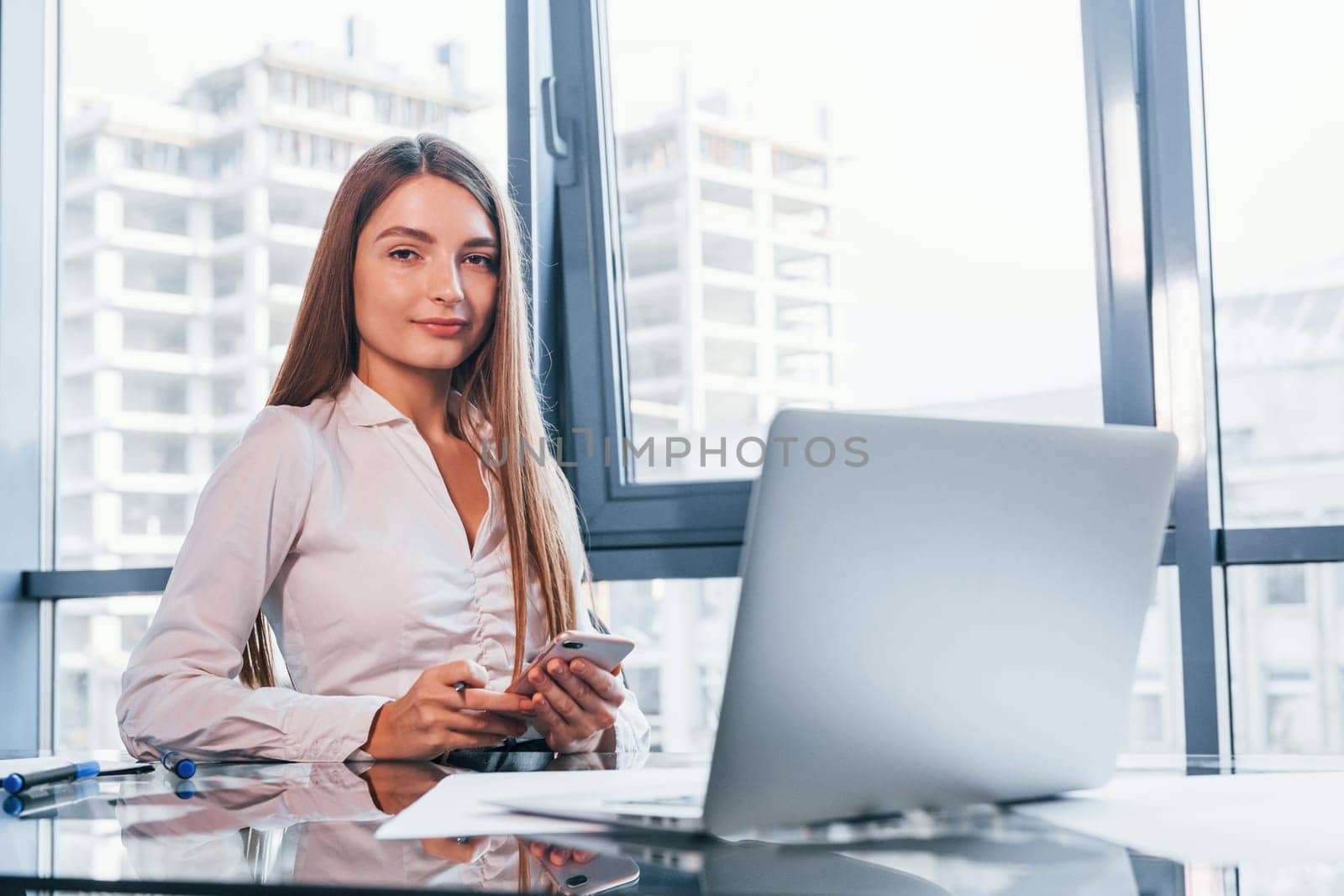 Young woman in white formal clothes is indoors in the modern office.