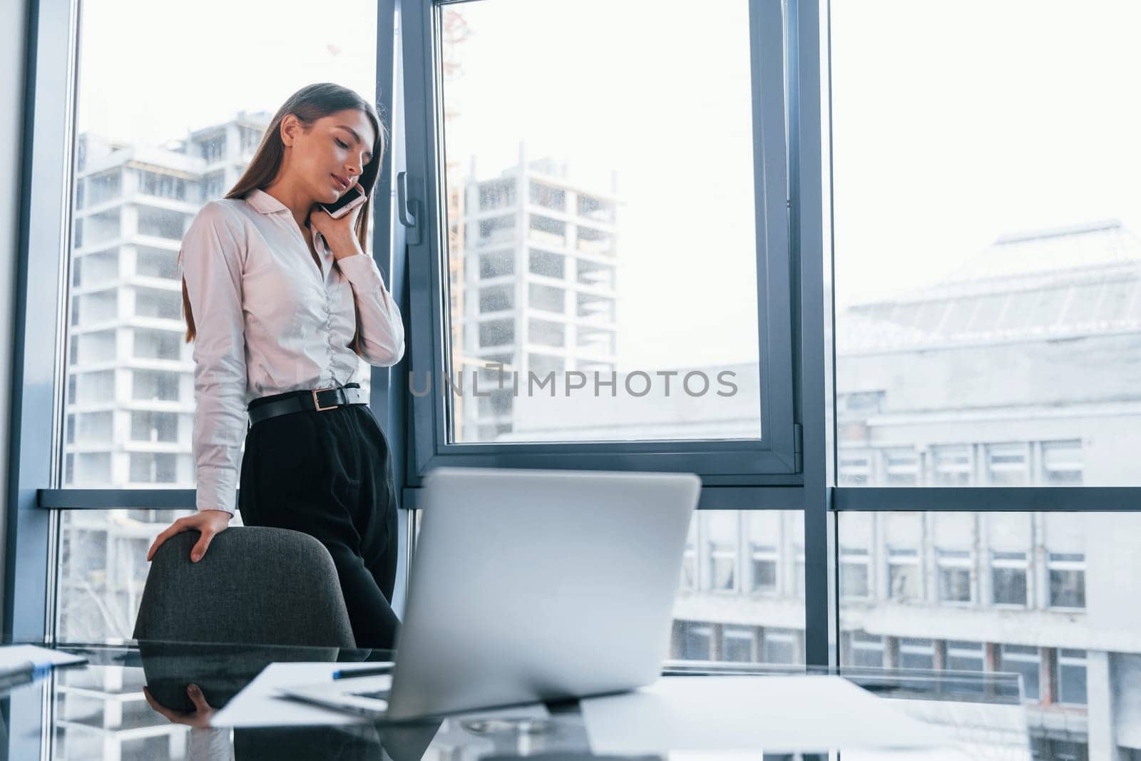 Young woman in white formal clothes is indoors in the modern office.
