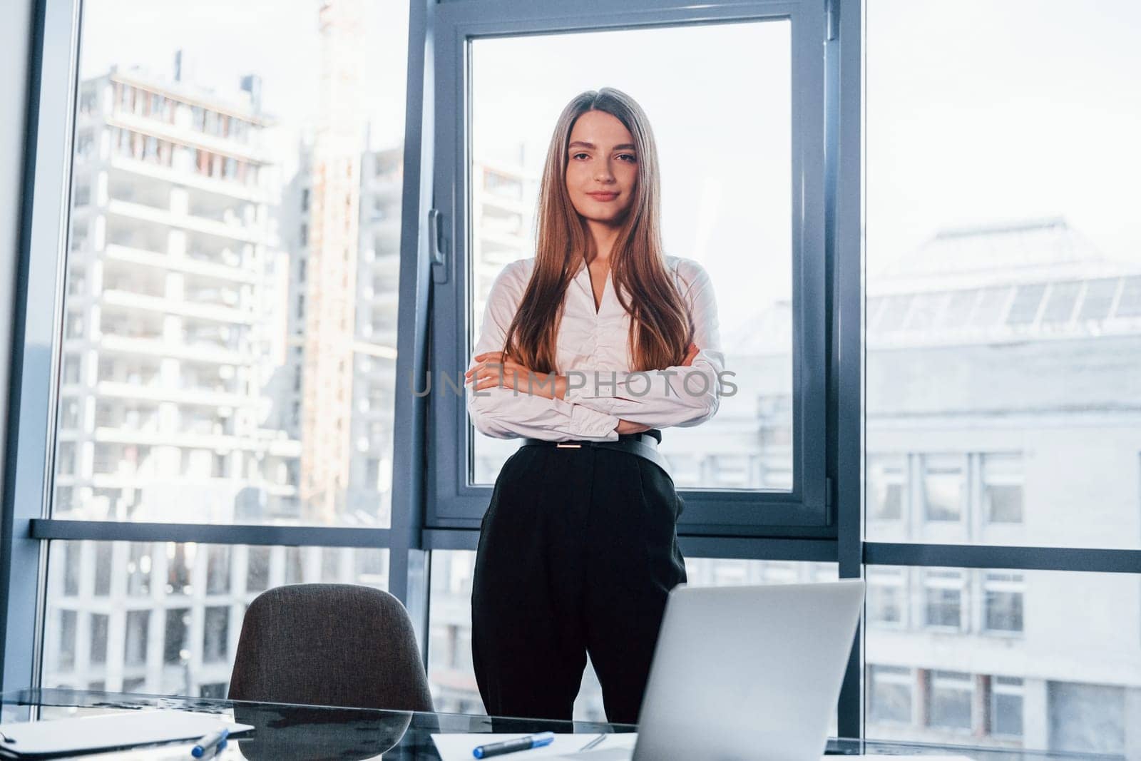 Young woman in white formal clothes is indoors in the modern office.