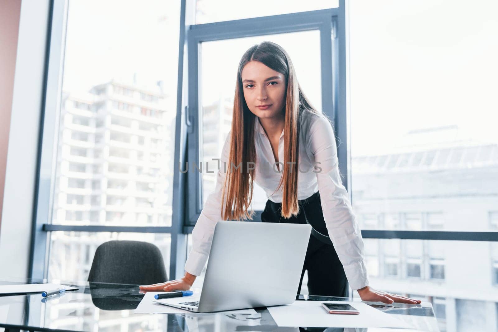 Young woman in white formal clothes is indoors in the modern office.