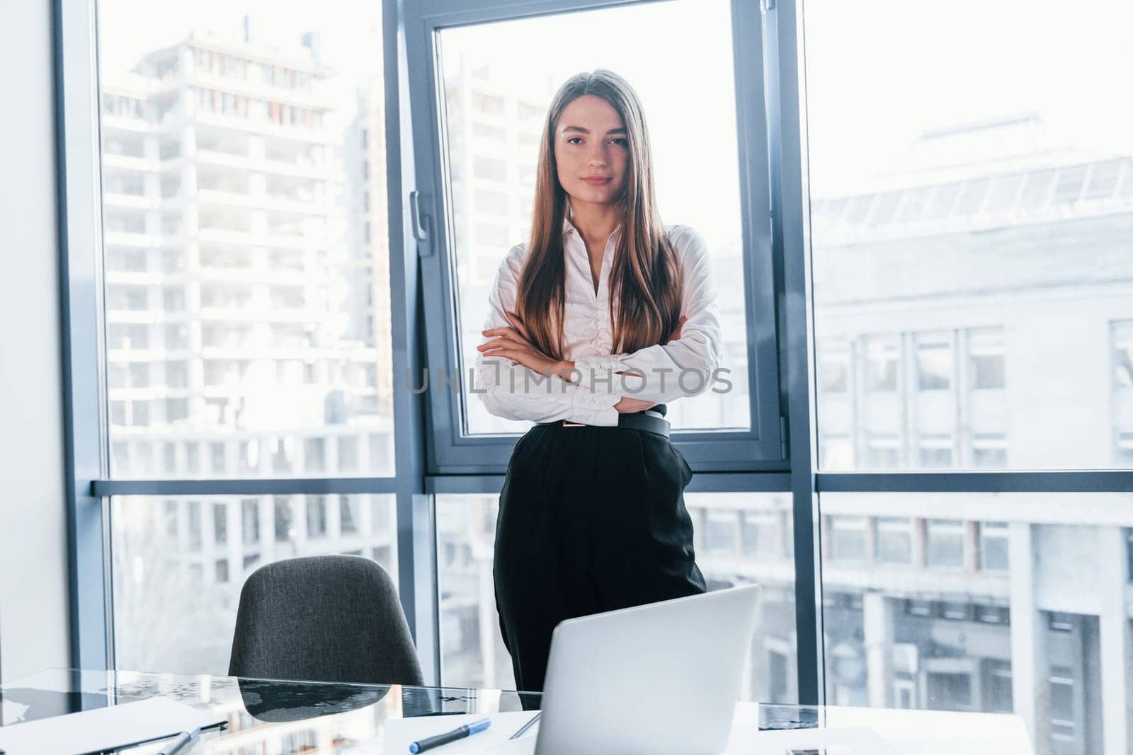 Young woman in white formal clothes is indoors in the modern office.