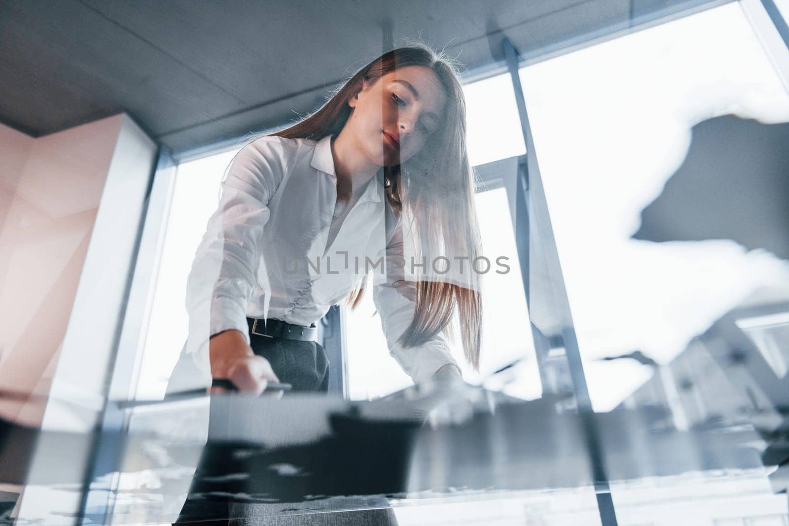 View from below. Young woman in white formal clothes is indoors in the modern office.