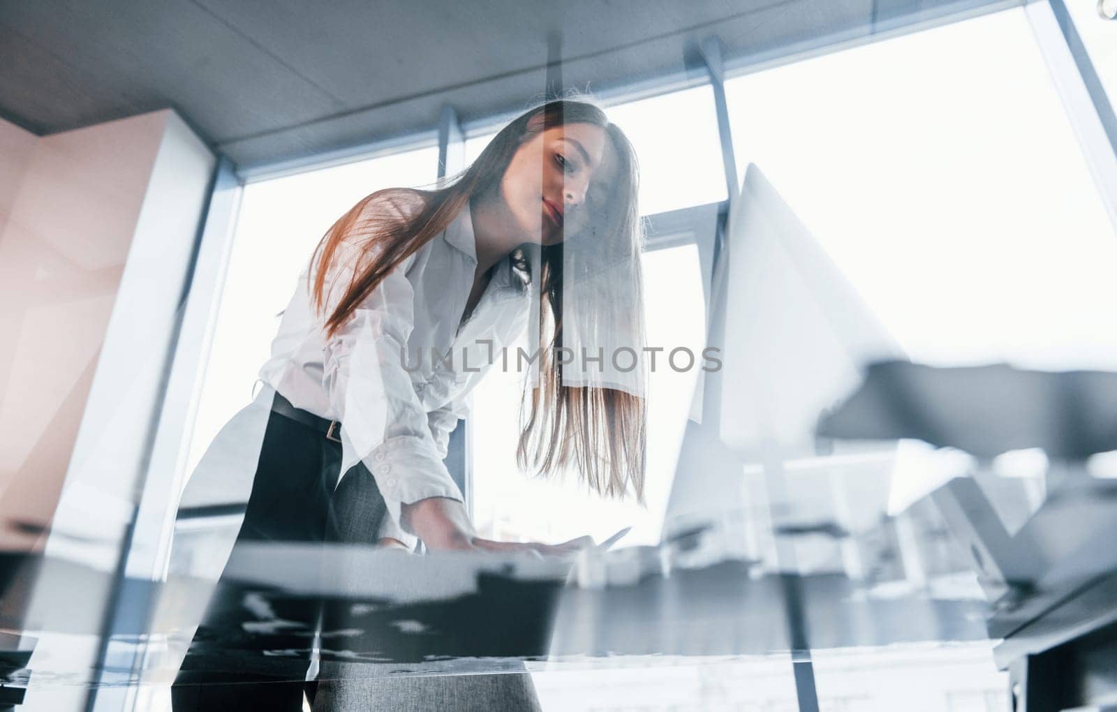 View from below. Young woman in white formal clothes is indoors in the modern office.