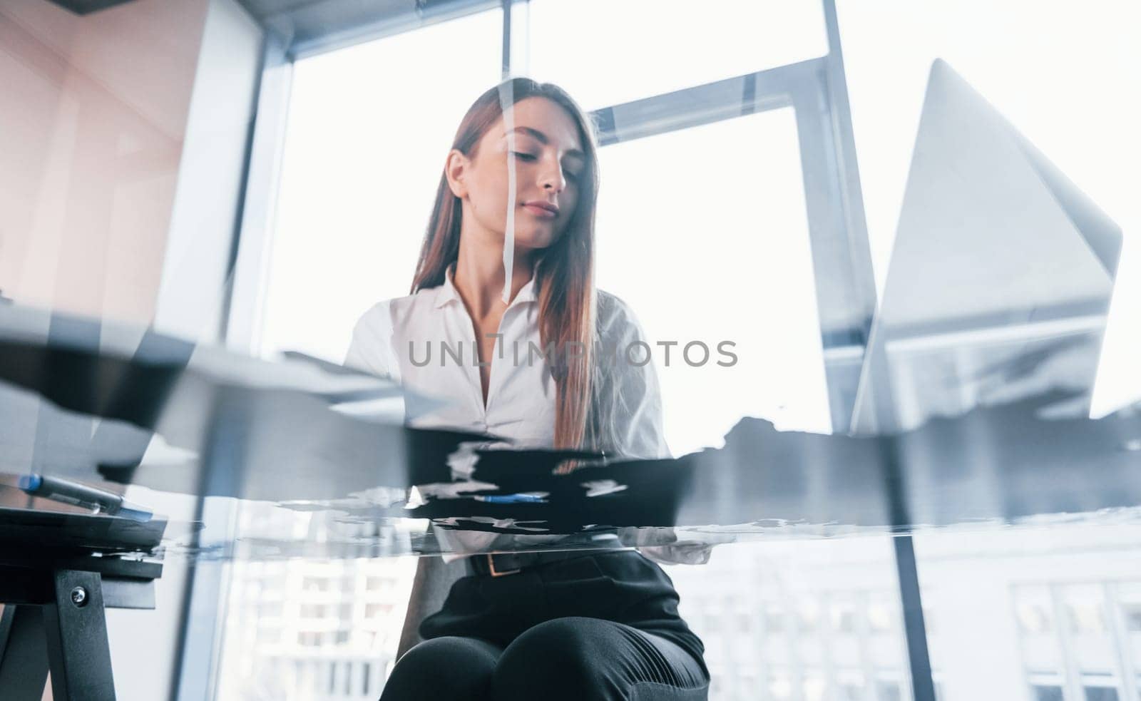 Busy day. Young woman in white formal clothes is indoors in the modern office.