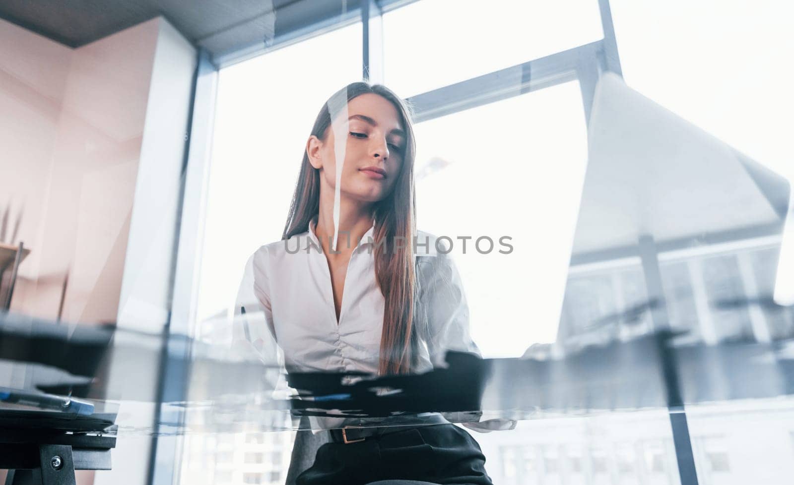Busy day. Young woman in white formal clothes is indoors in the modern office.