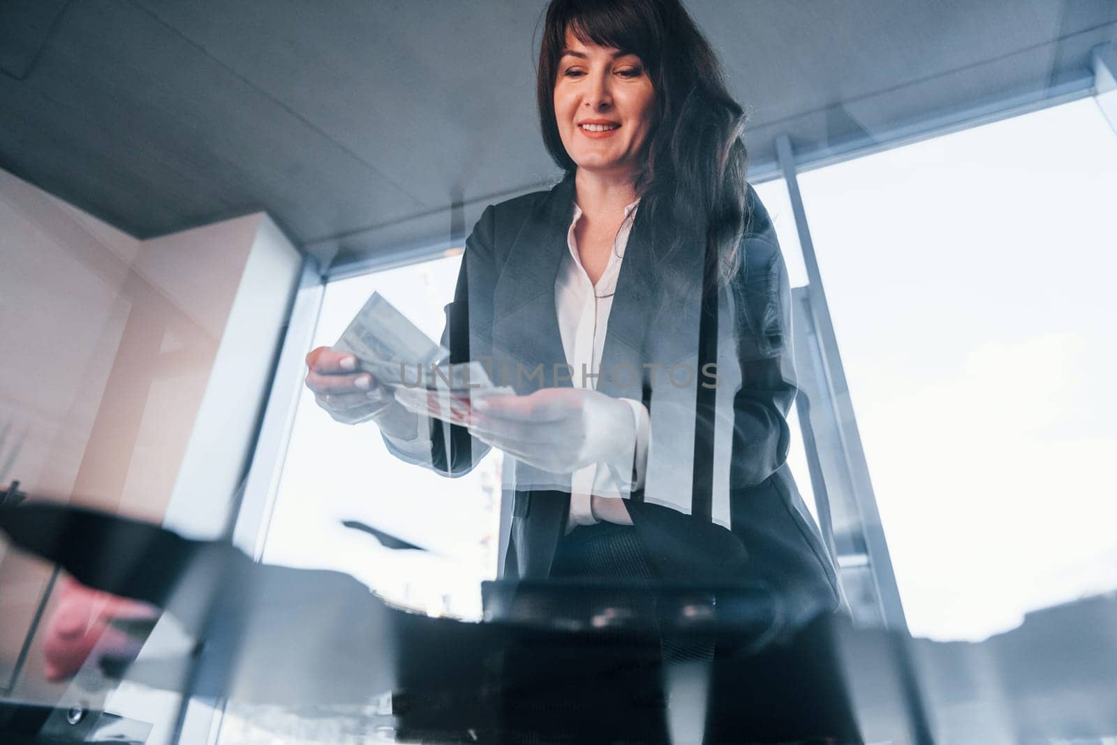Woman in black formal clothes is indoors in the modern office.