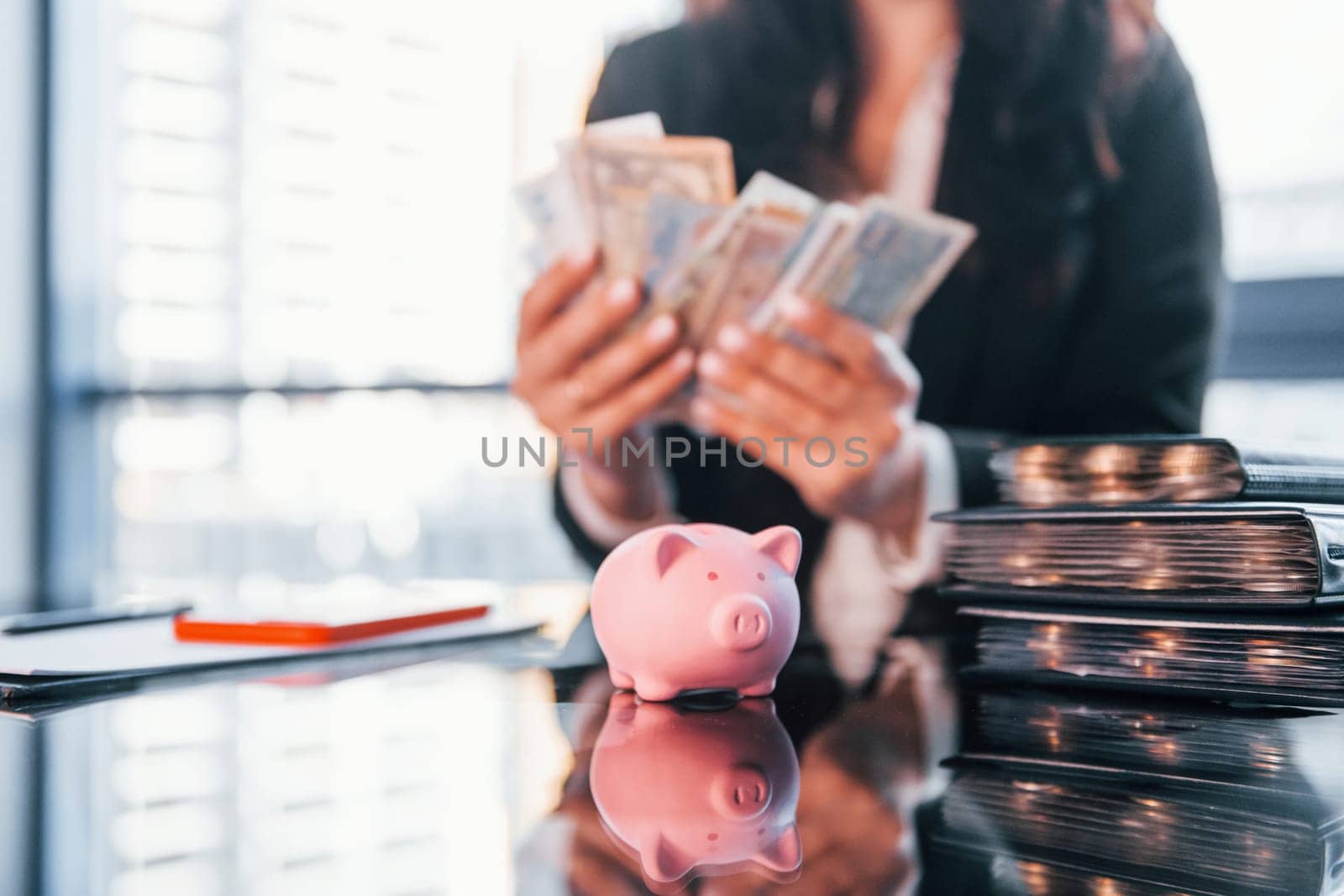 With currency. Woman in black formal clothes is indoors in the modern office.