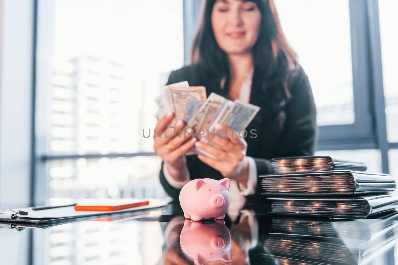 With currency. Woman in black formal clothes is indoors in the modern office.