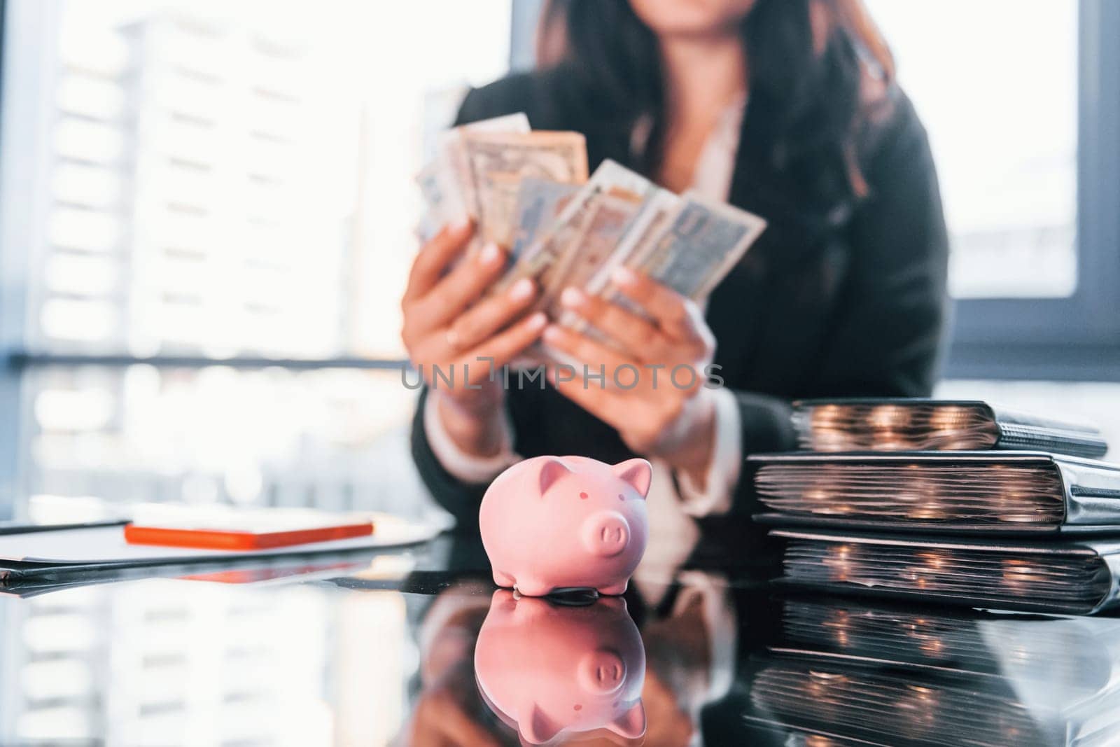 With currency. Woman in black formal clothes is indoors in the modern office.