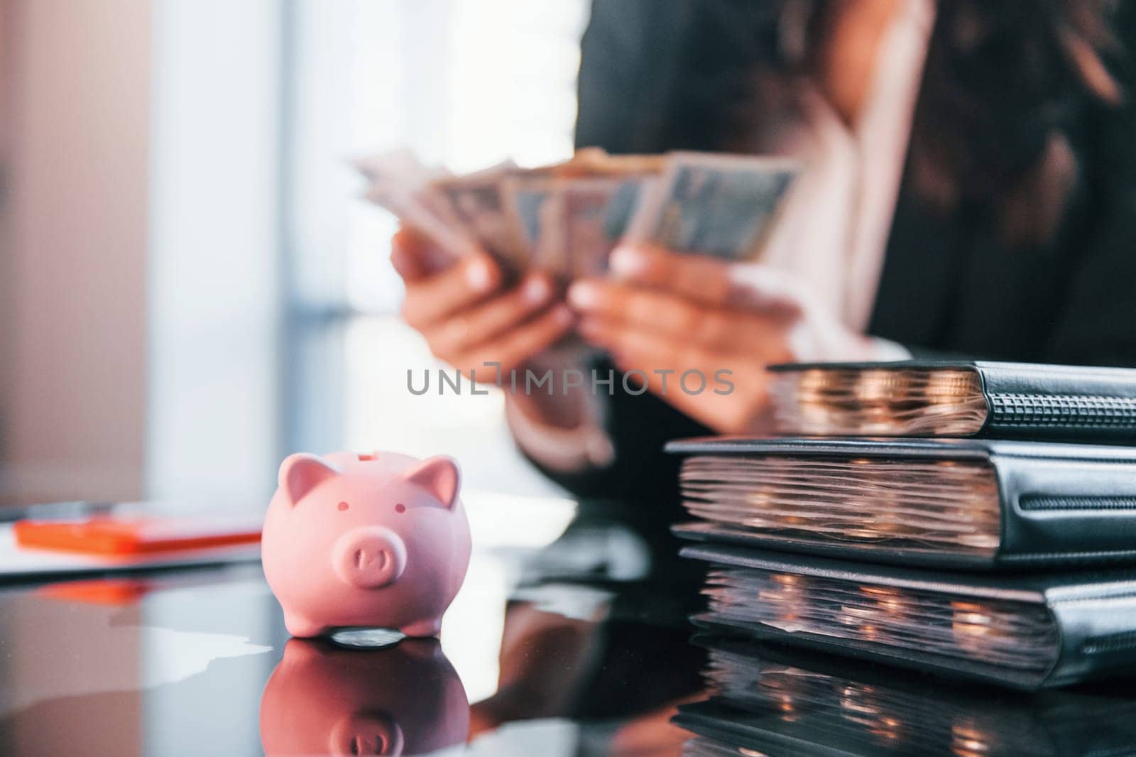 With currency. Woman in black formal clothes is indoors in the modern office.