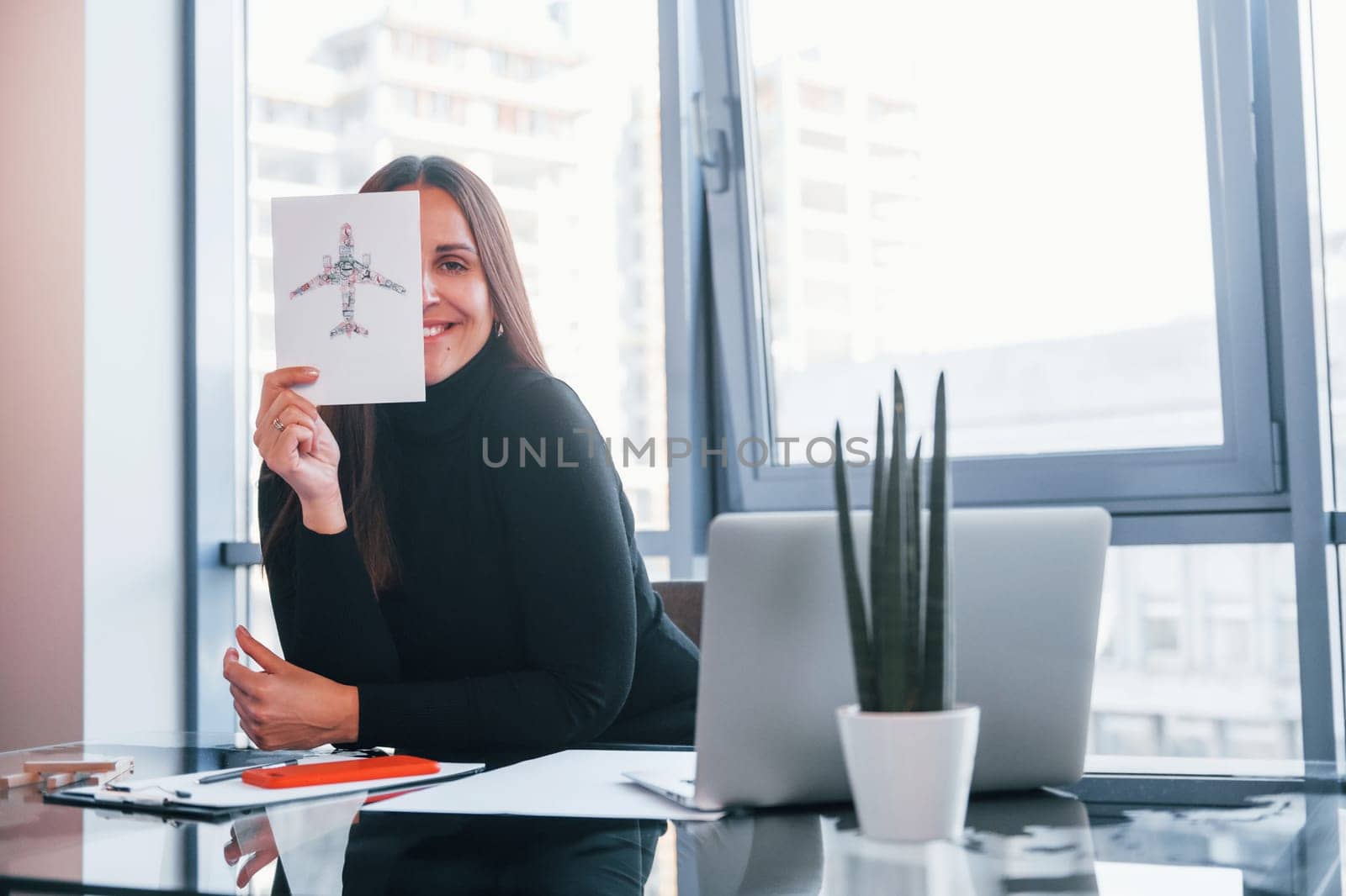 With laptop on table. Woman in black formal clothes is indoors in the modern office.