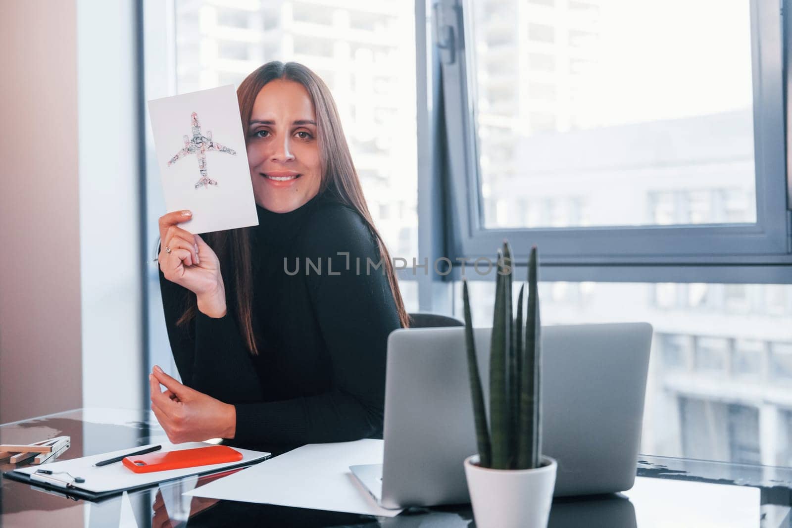 With laptop on table. Woman in black formal clothes is indoors in the modern office.