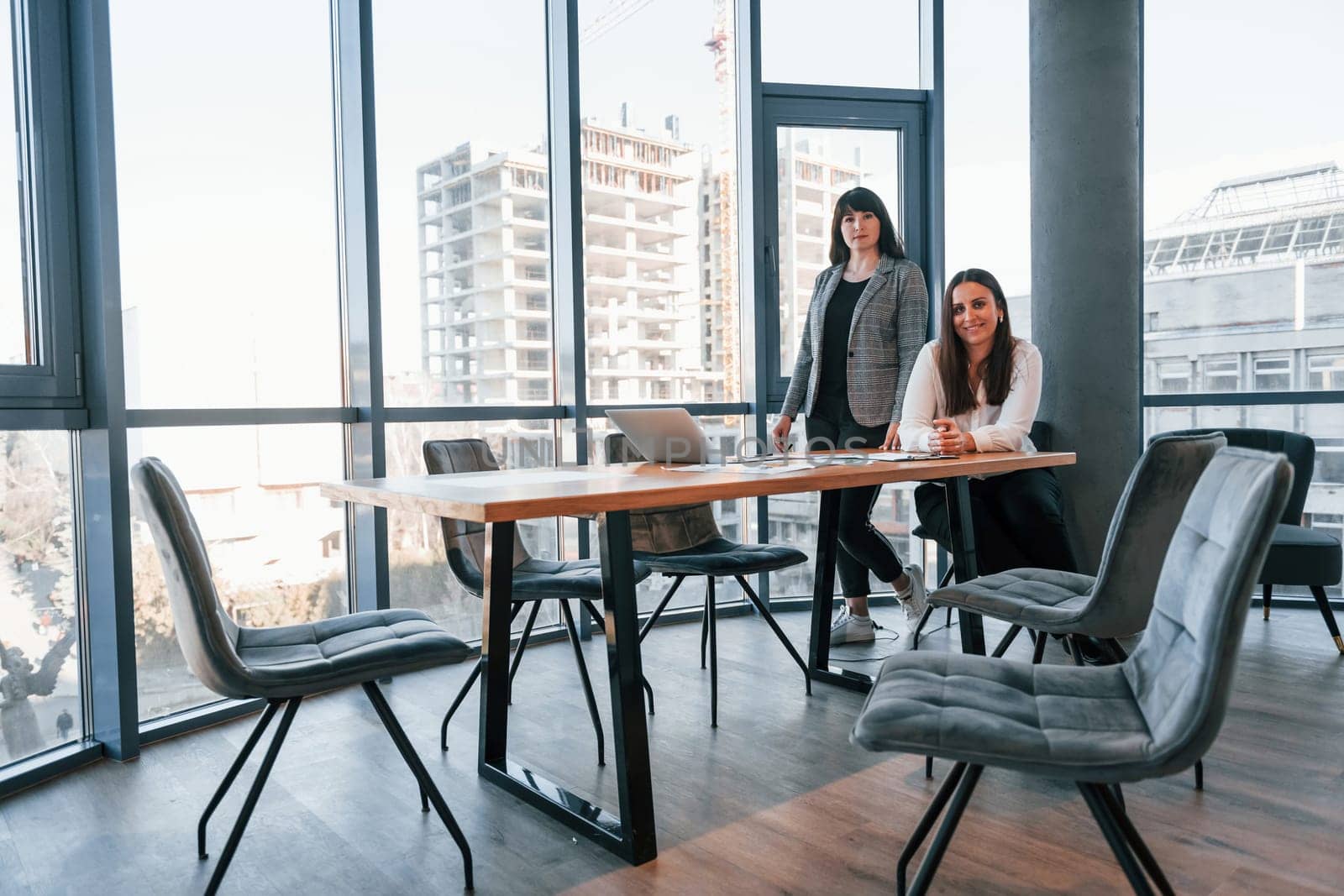 Two women in formal clothes is indoors in the modern office works together.