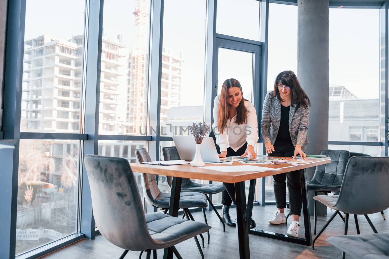 Standing and talking. Two women in formal clothes is indoors in the modern office works together.