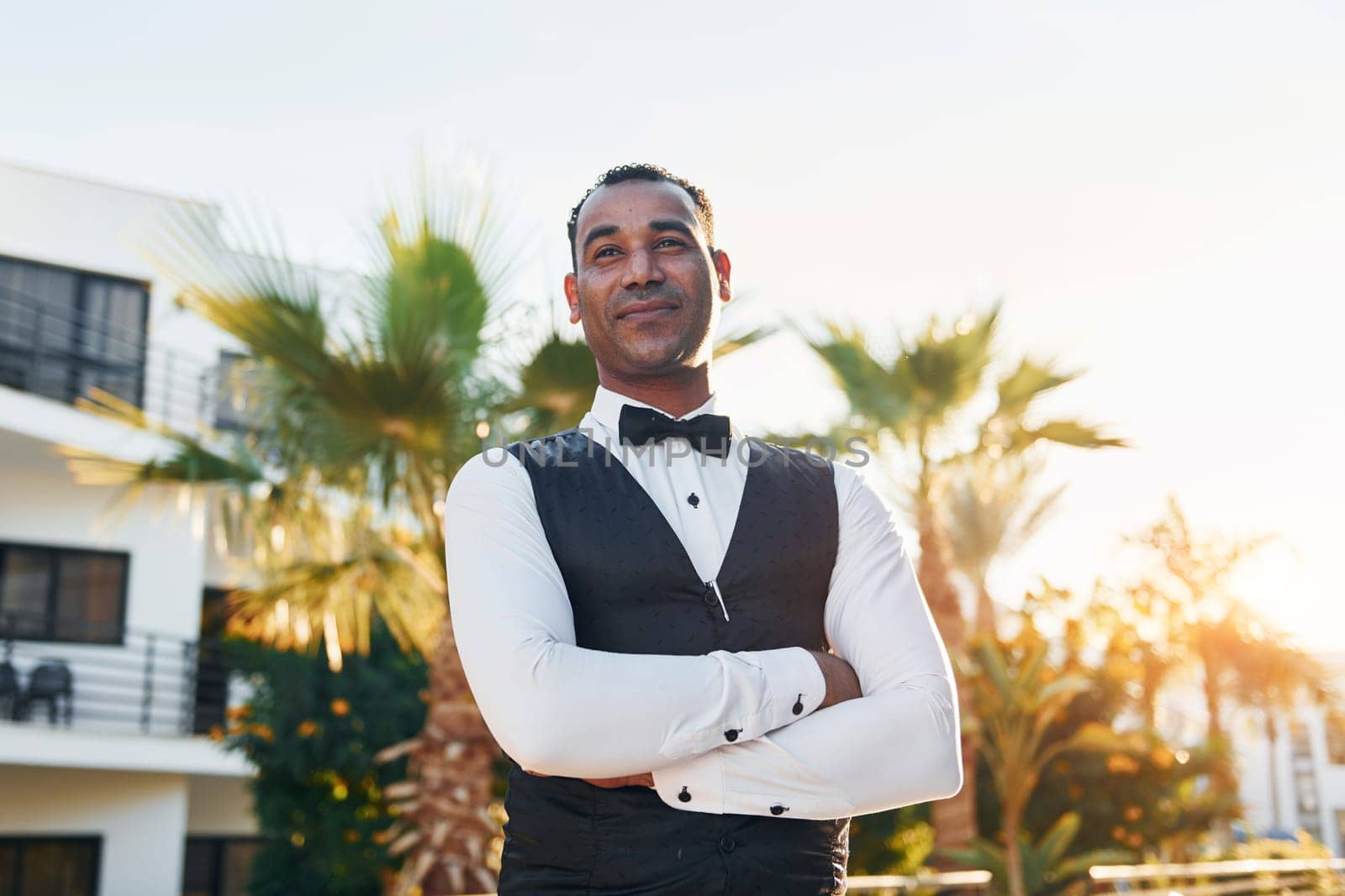 Posing for a camera. Black waiter in formal clothes is at his work outdoors at sunny daytime.