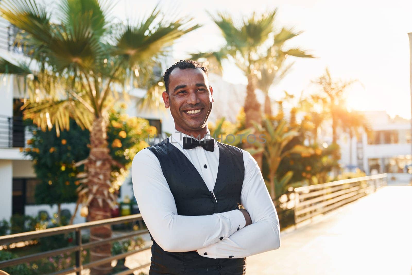 Posing for a camera. Black waiter in formal clothes is at his work outdoors at sunny daytime.