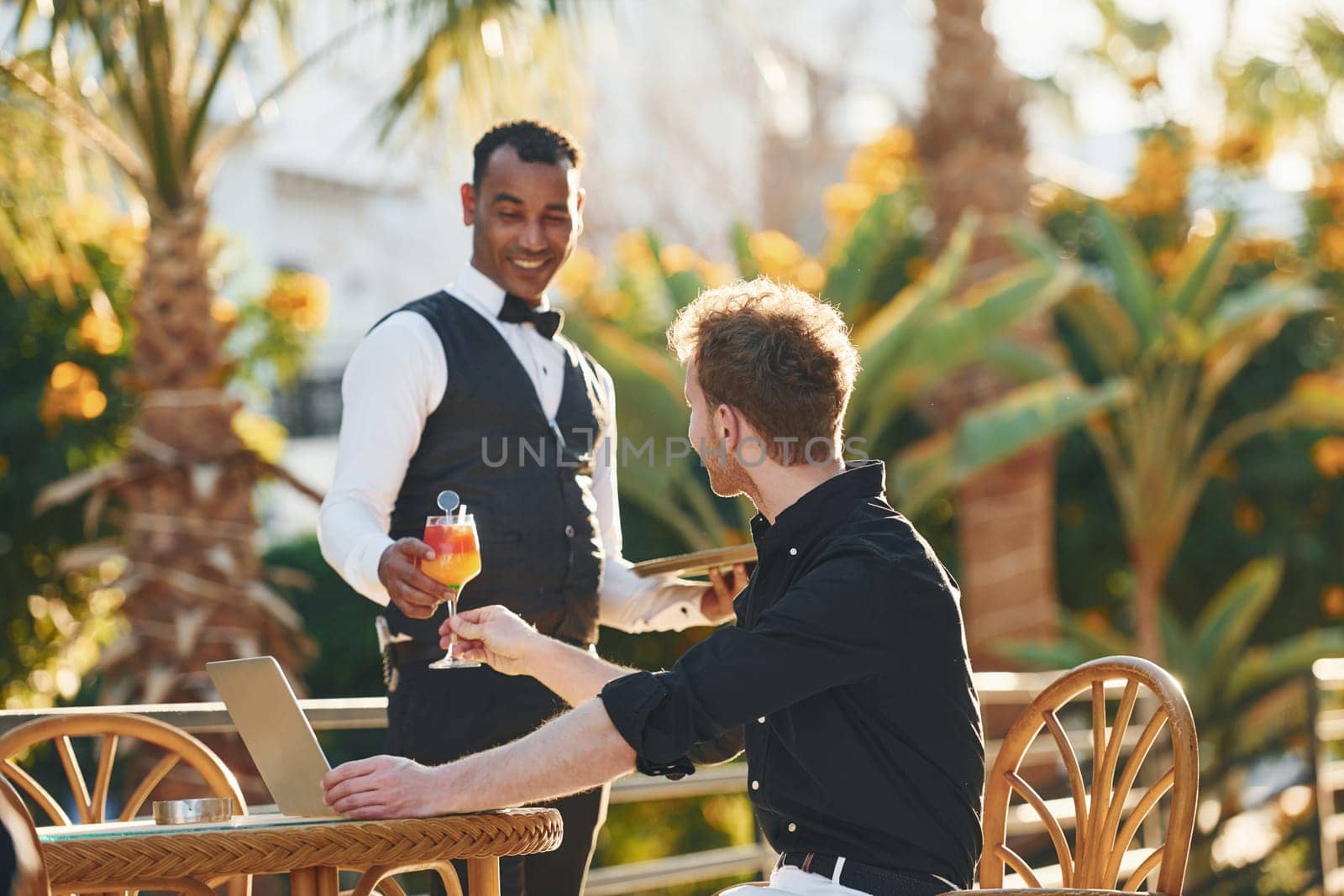 Serviced by waiter. Young man is outdoors at sunny daytime. Concept of vacation by Standret