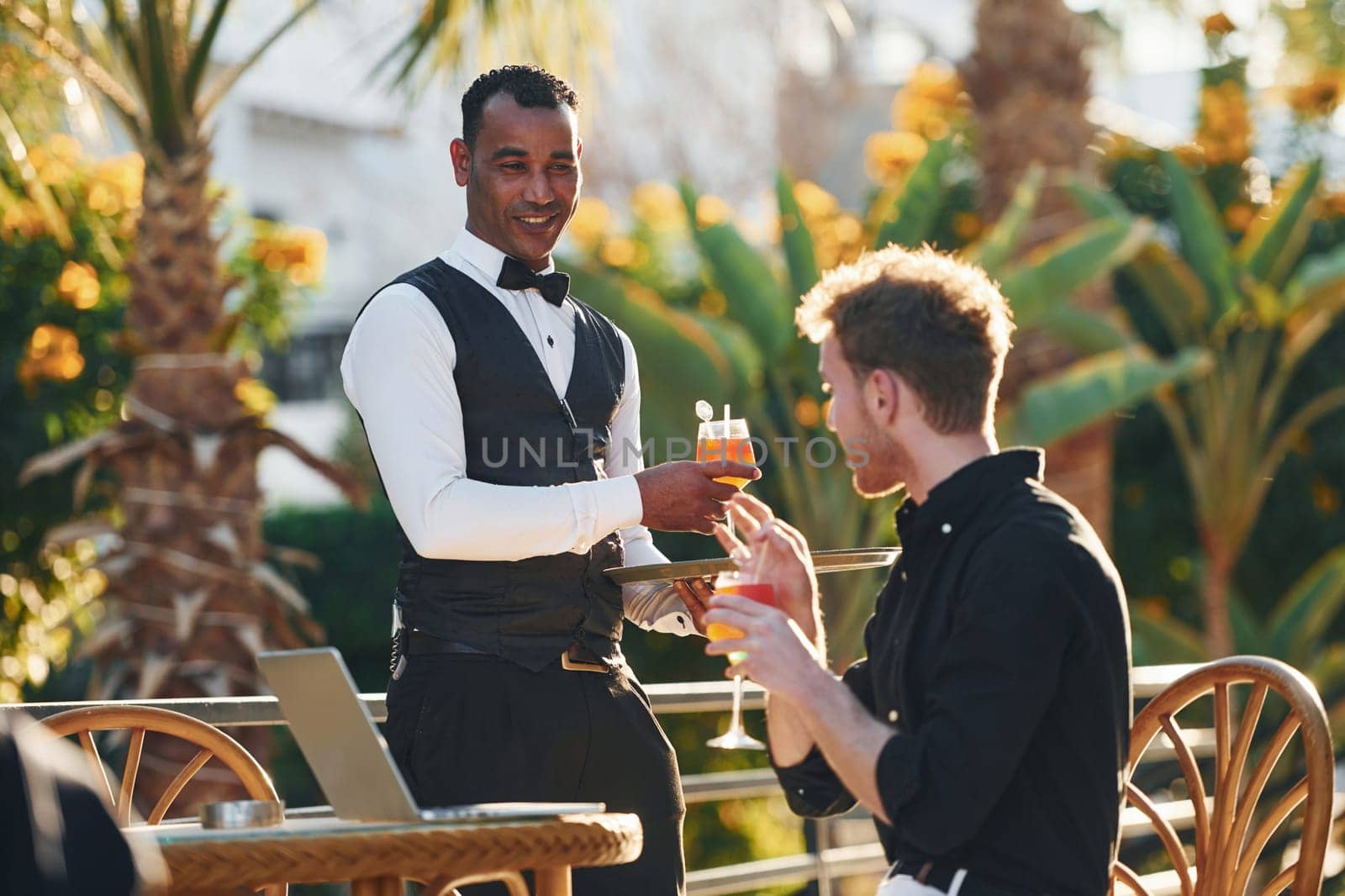 Serviced by waiter. Young man is outdoors at sunny daytime. Concept of vacation by Standret