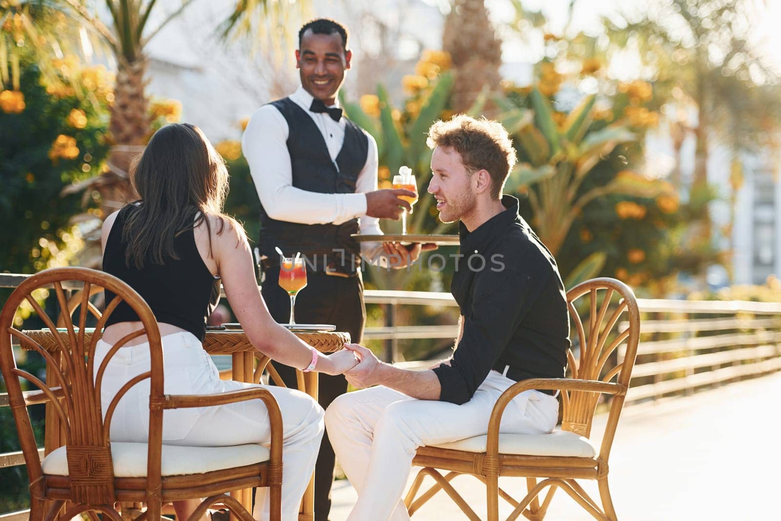 Serviced by waiter. Happy young couple is together on their vacation. Outdoors at sunny daytime.