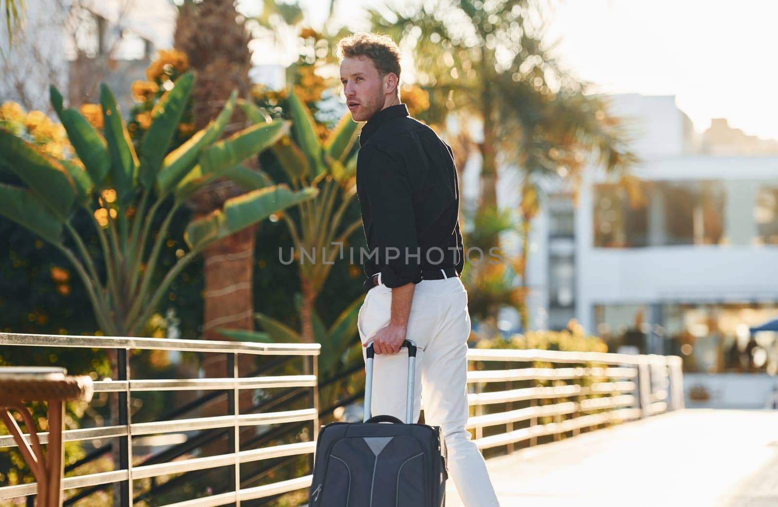 With travel bag. Young man is outdoors at sunny daytime. Concept of vacation.