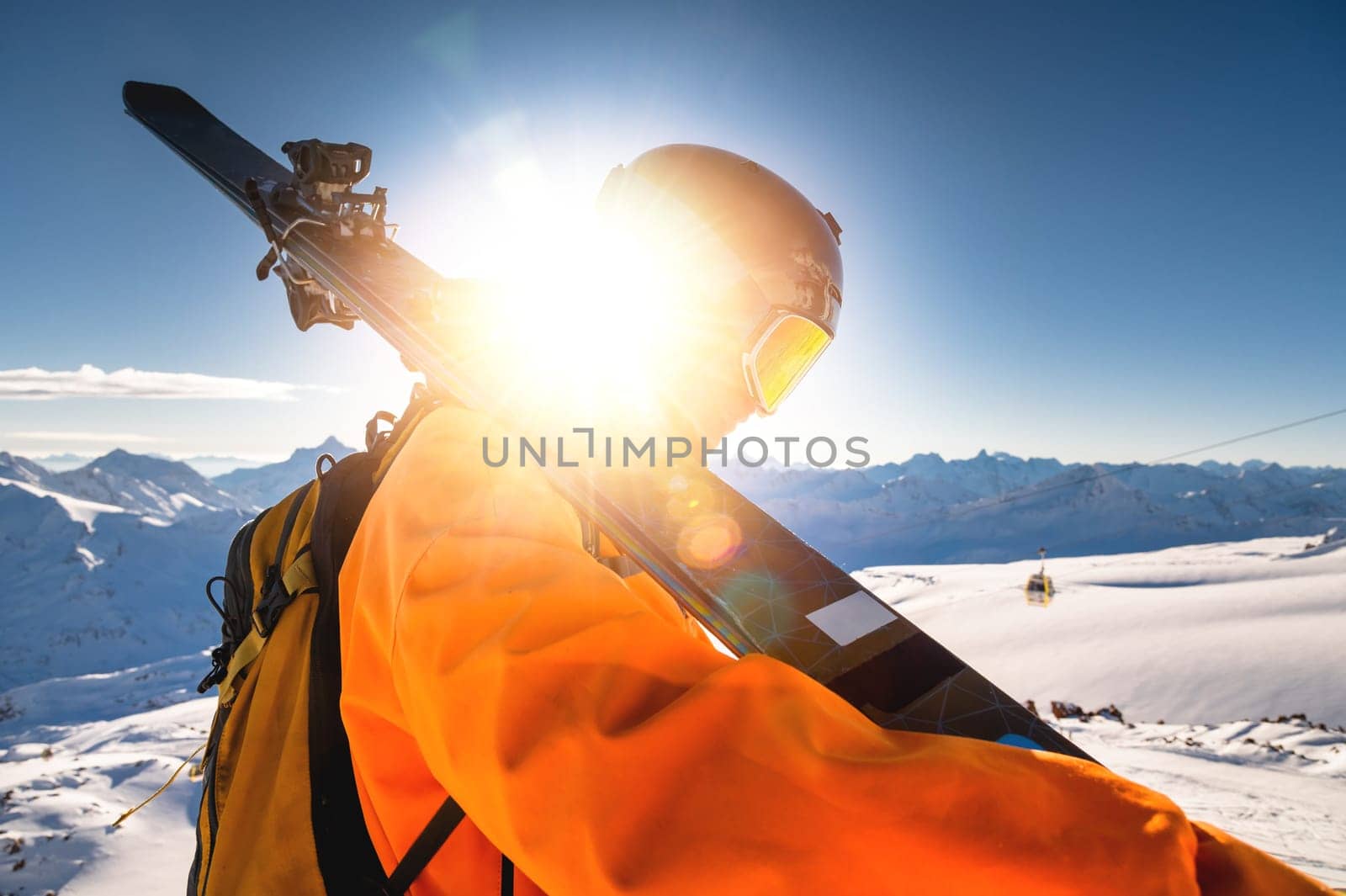 The skier stands on the top of the mountain and enjoys the view of the beautiful winter mountains on a sunny day. Man holding skis on his shoulder by yanik88