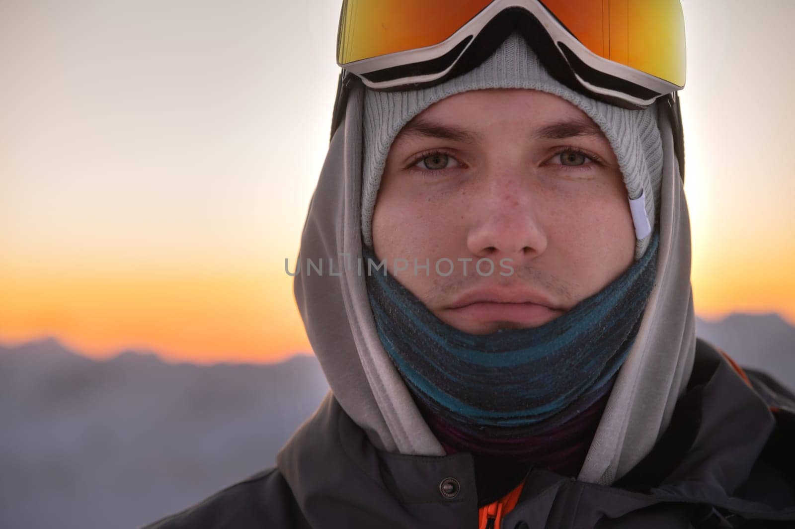 Portrait of a pensive skier in the mountains at sunset. A young man looks at the camera while standing in ski goggles against the backdrop of a sunset sky in the mountains by yanik88