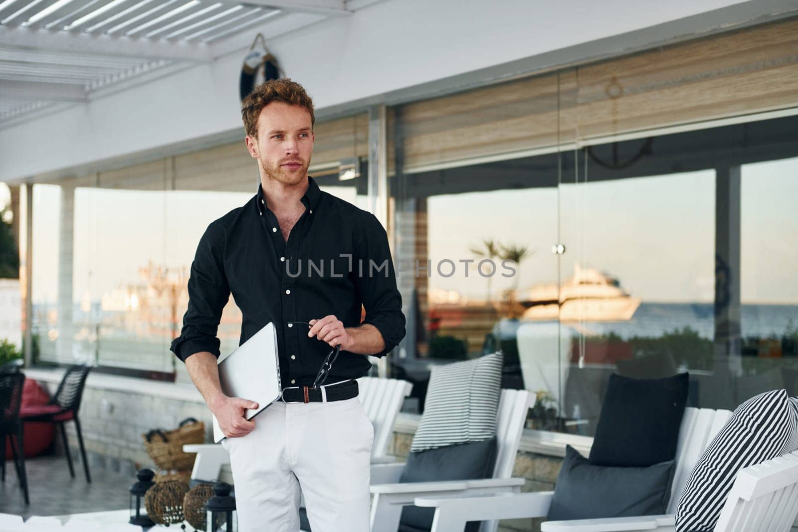 Holds laptop. Young man is outdoors at sunny daytime. Concept of vacation.