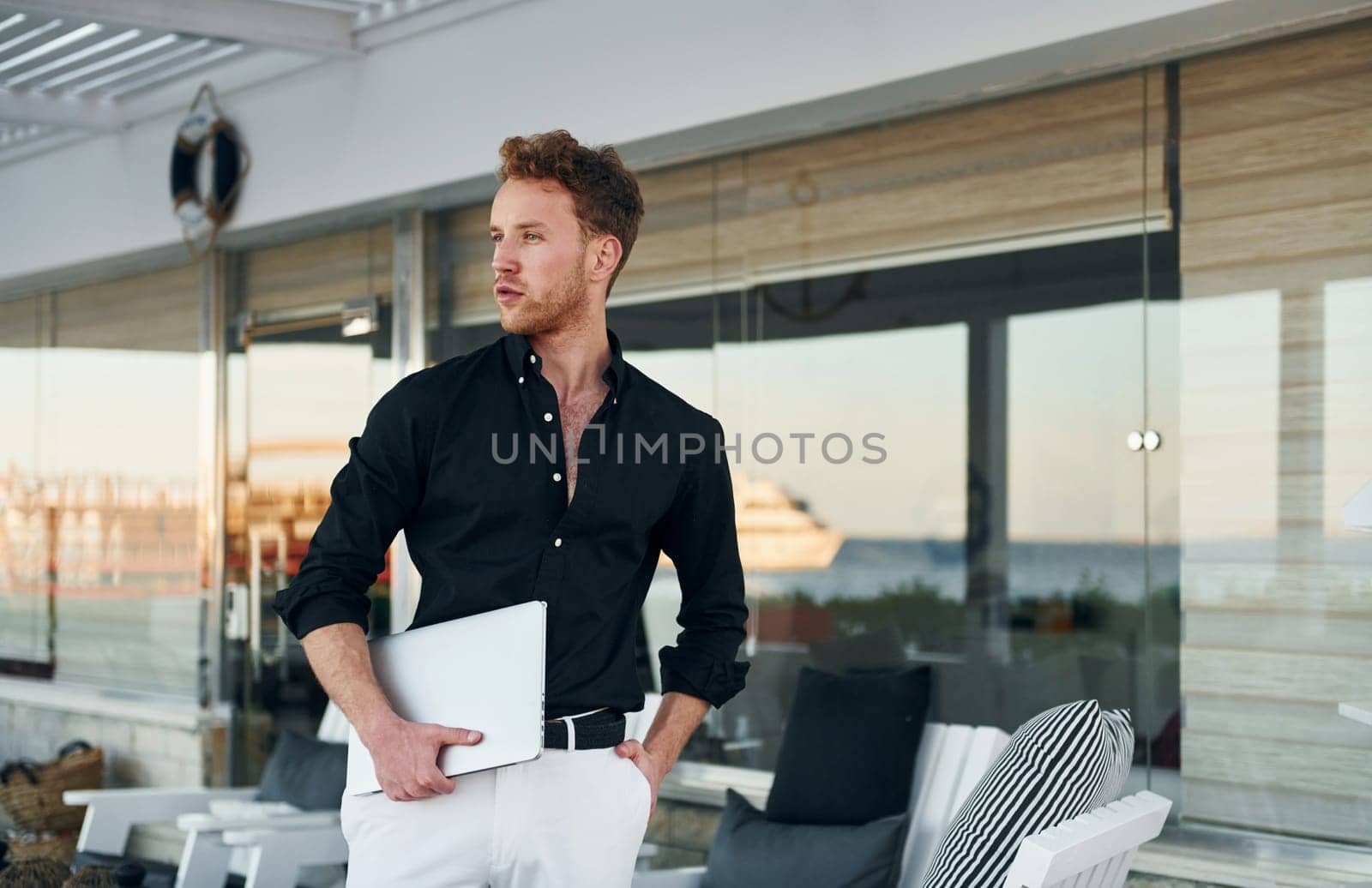 Holds laptop. Young man is outdoors at sunny daytime. Concept of vacation.