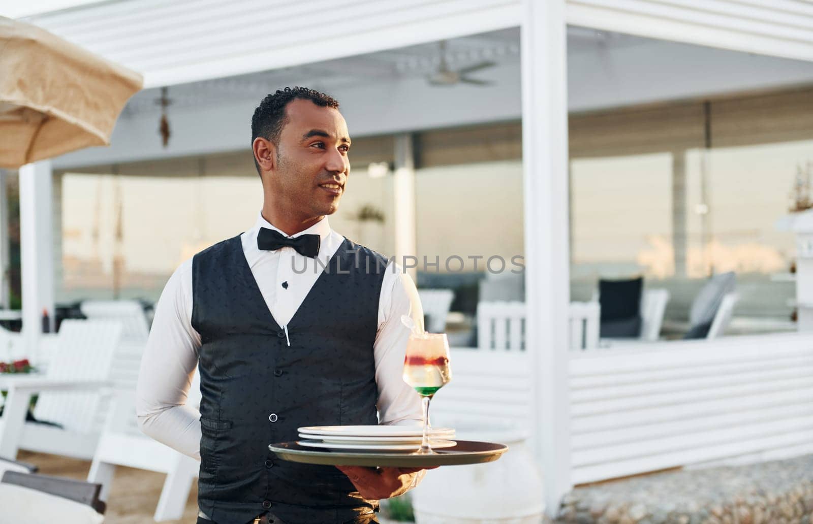 With order in hand. Black waiter in formal clothes is at his work outdoors at sunny daytime.