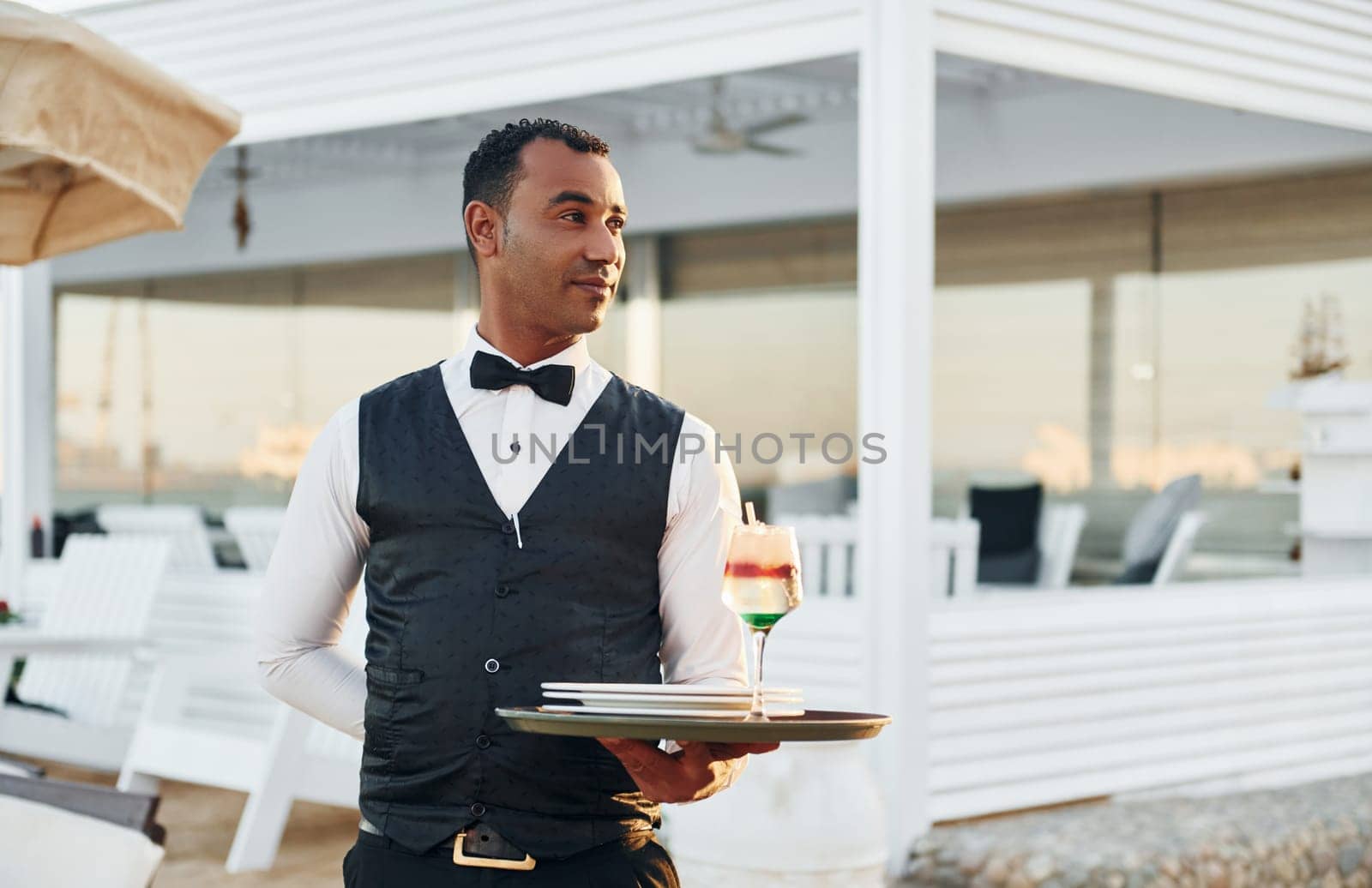 With order in hand. Black waiter in formal clothes is at his work outdoors at sunny daytime.
