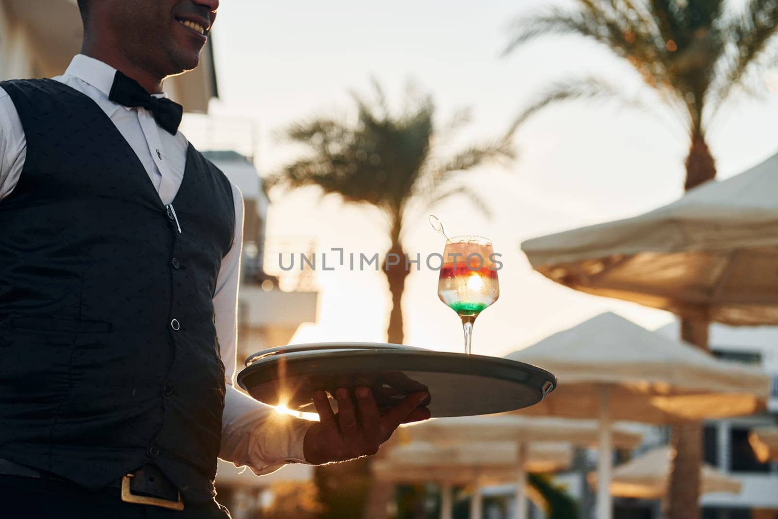 Close up view of drink. Black waiter in formal clothes is at his work outdoors at sunny daytime.