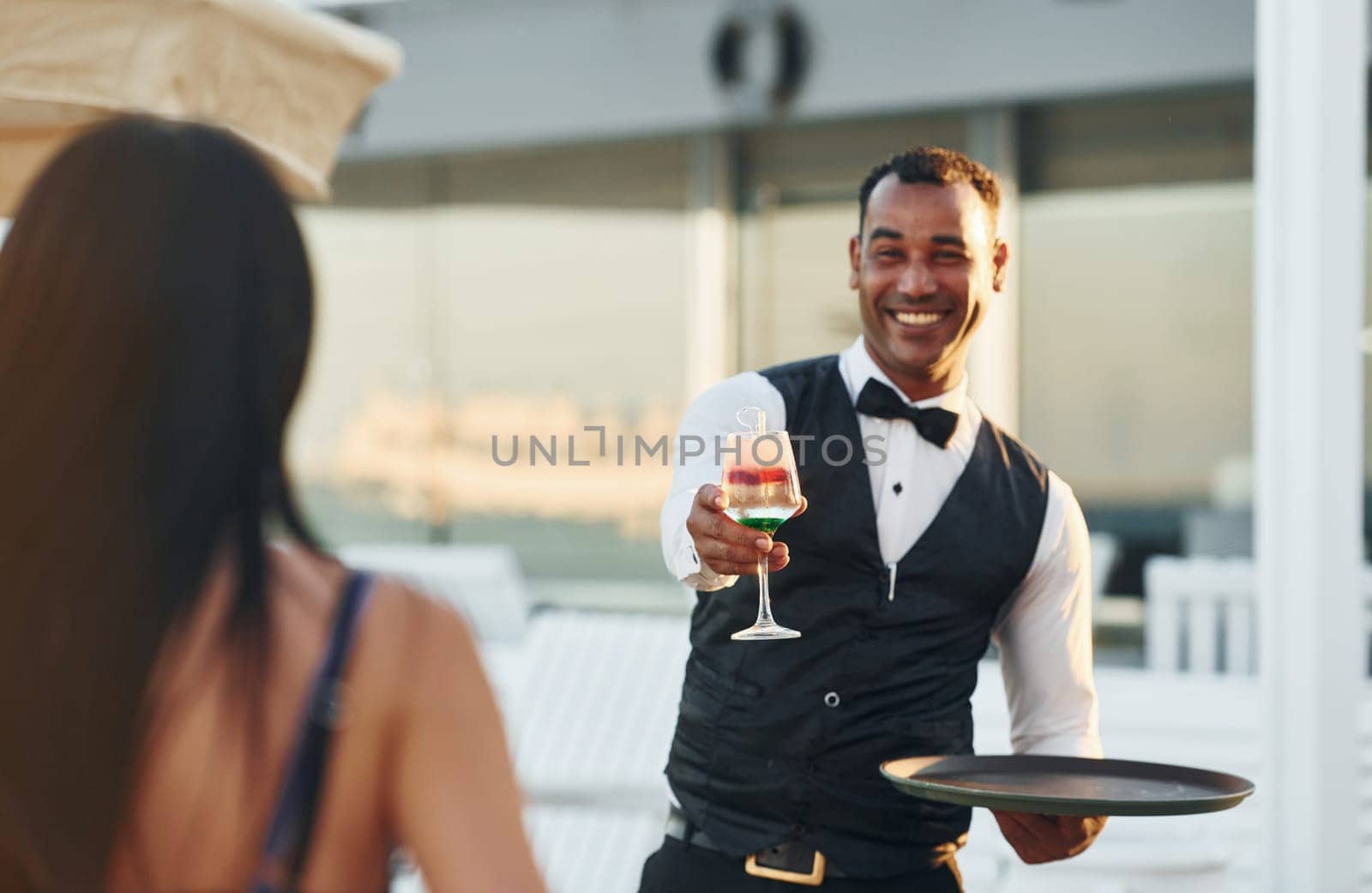 Order for woman. Black waiter in formal clothes is at his work outdoors at sunny daytime.