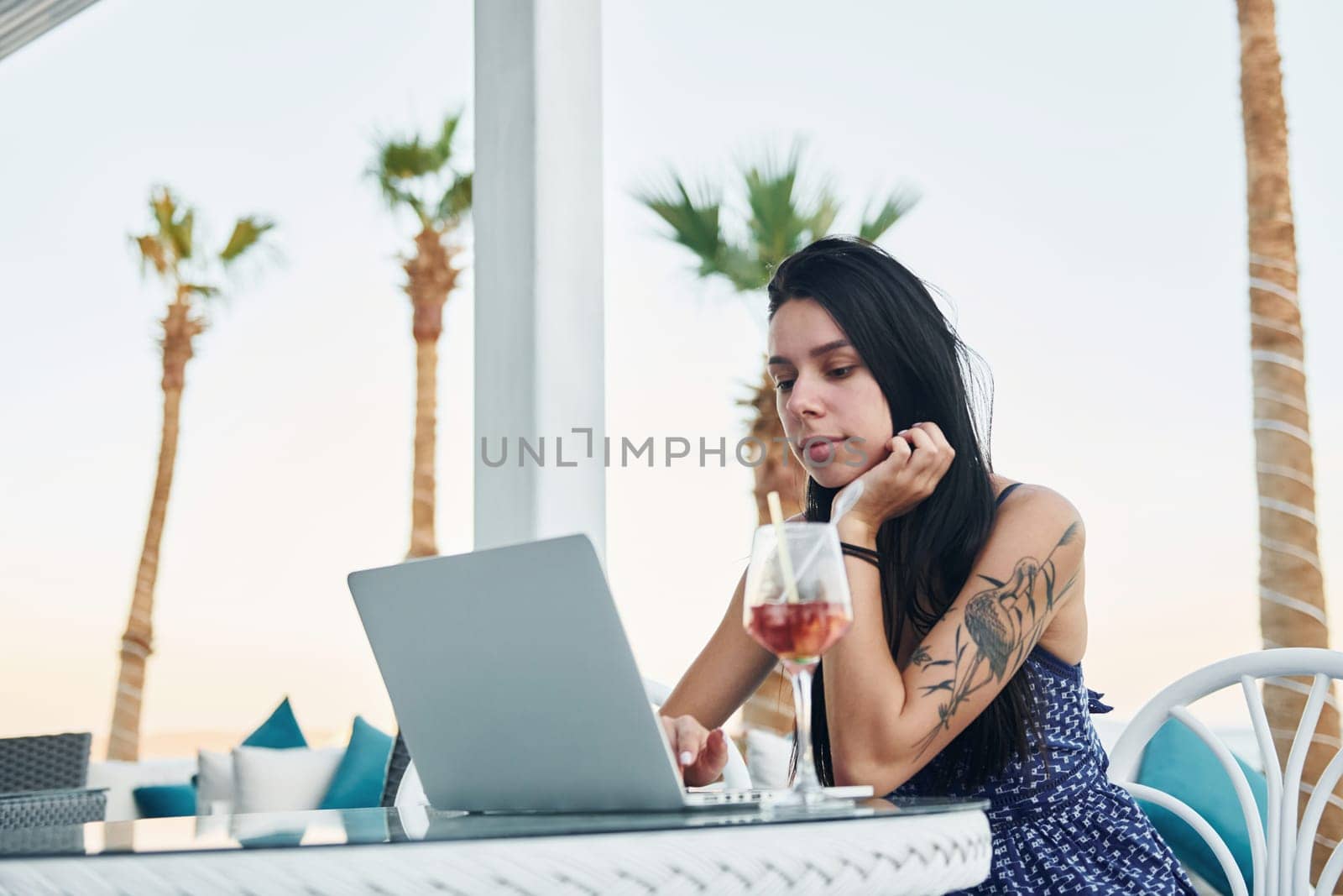 Uses laptop. Beautiful young woman is outdoors at sunny daytime. Concept of vacation.